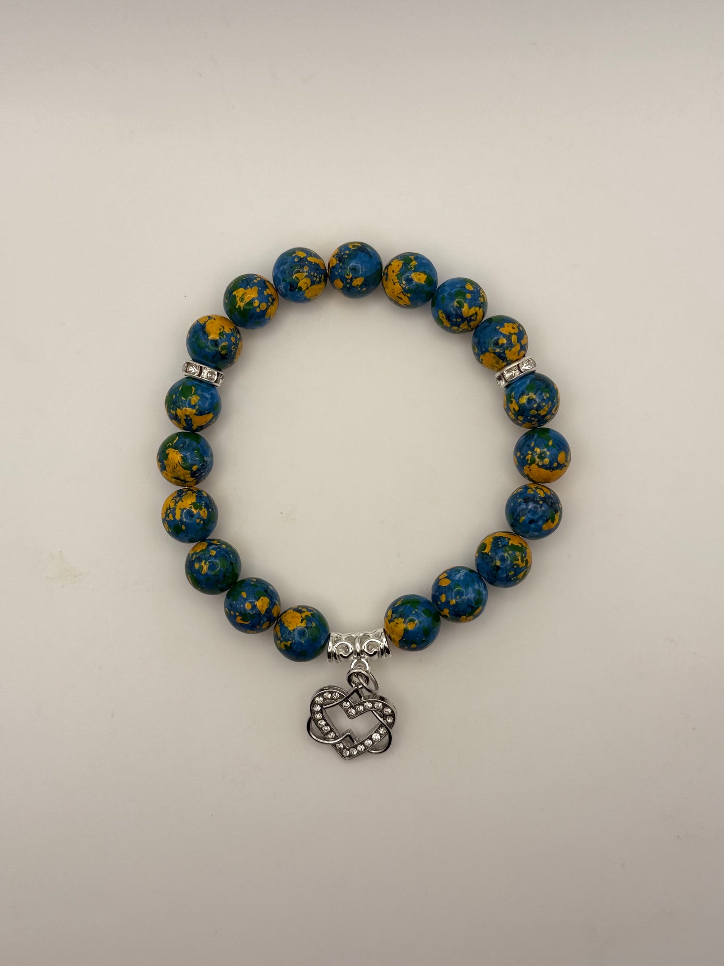Blue and yellow beaded bracelet with a silver charm on a light gray background
