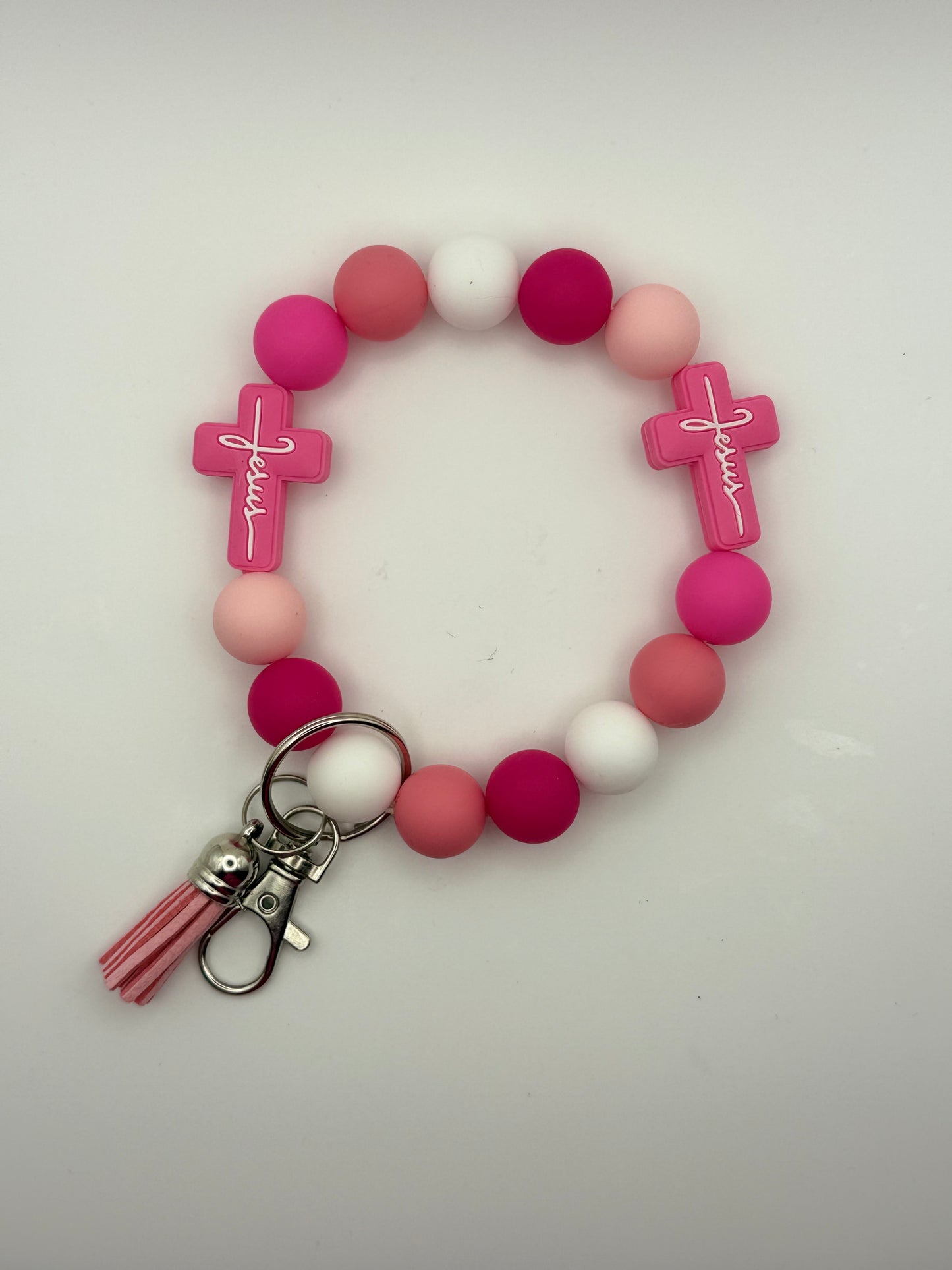 Pink beaded bracelet with cross charms and a keychain on a white background