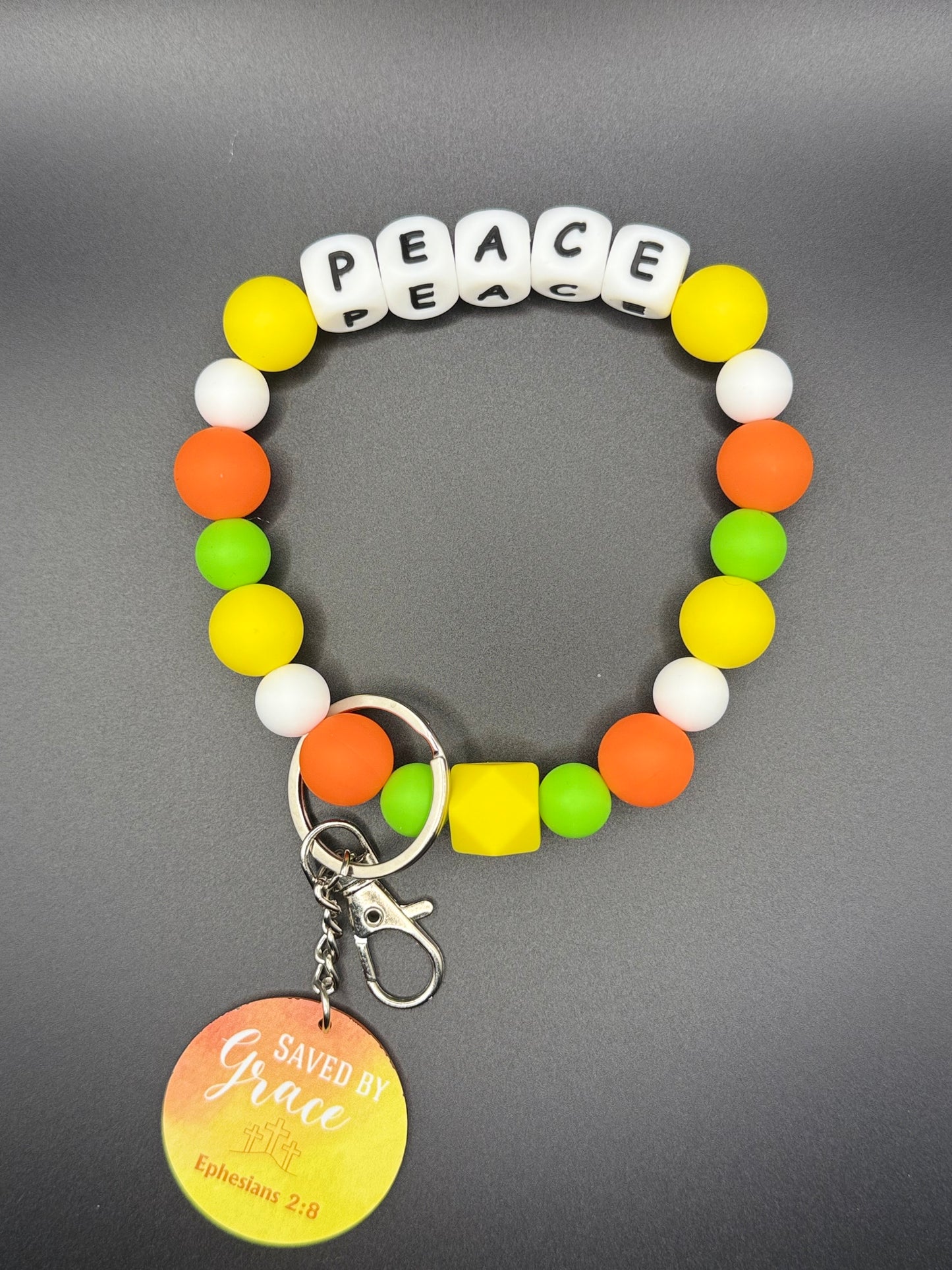 Colorful beaded bracelet with 'PEACE' charm on a gray background