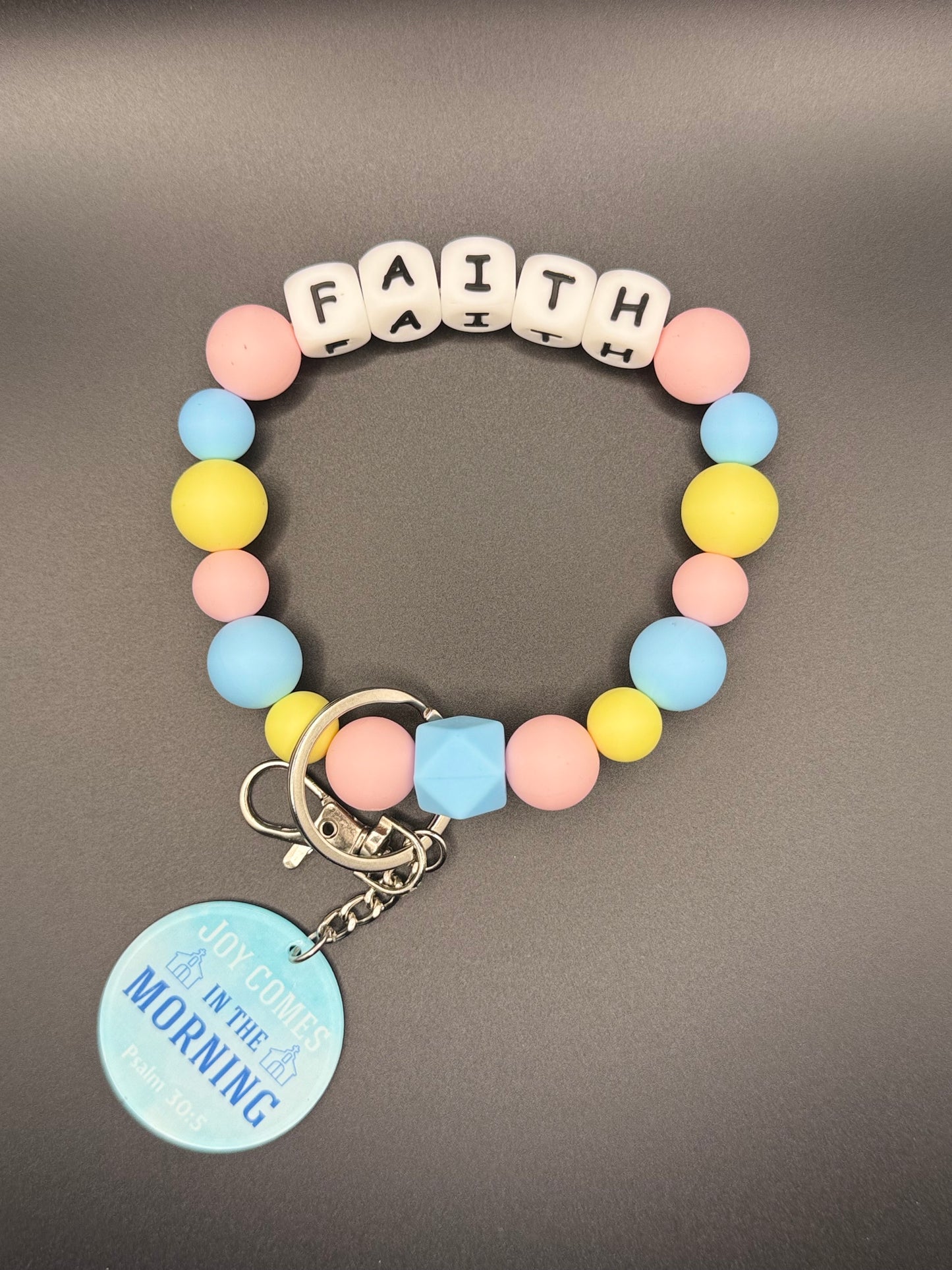 Colorful beaded bracelet with letter beads spelling 'FAITH' on a gray background