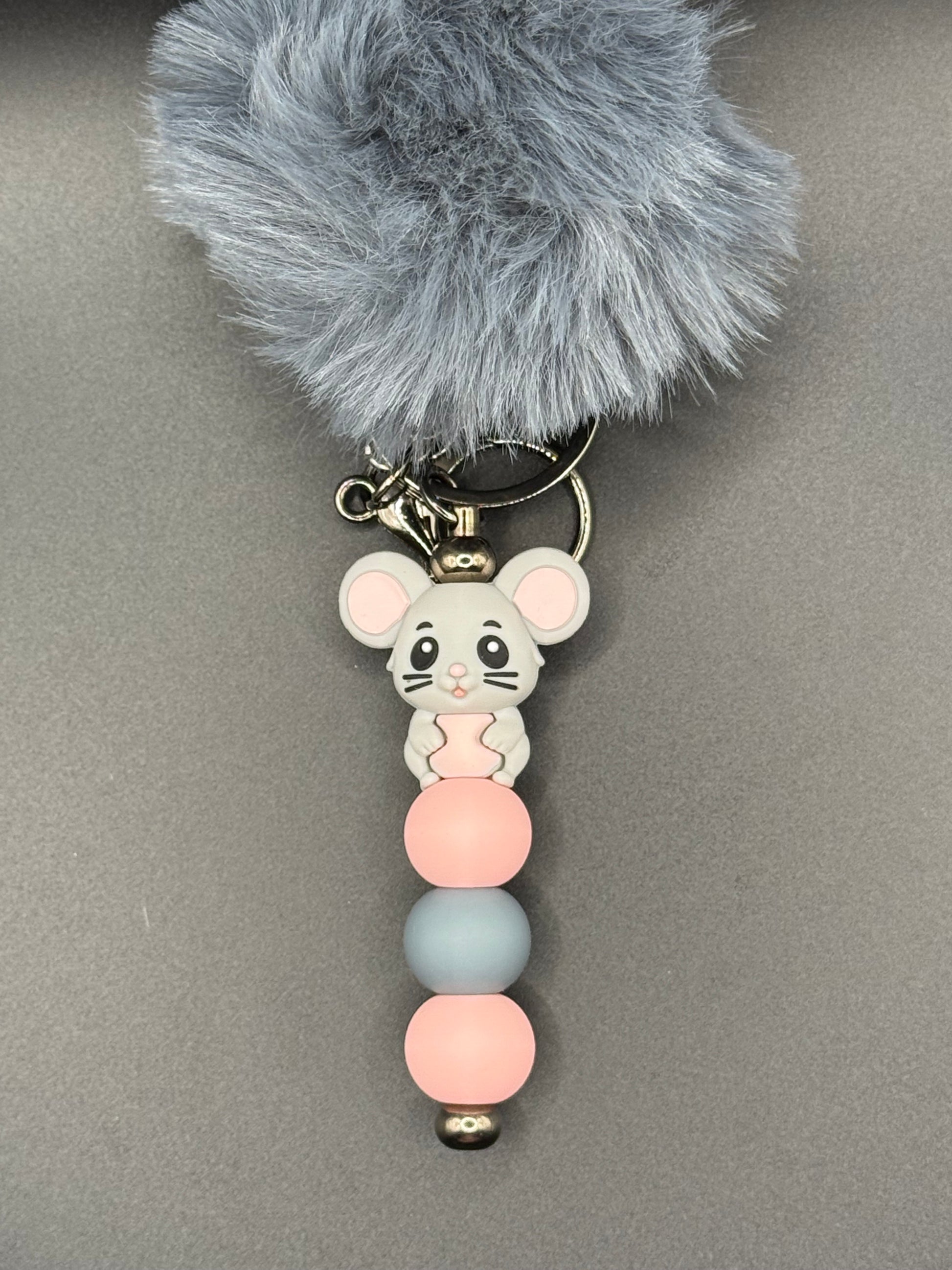 Keychain with gray fluffy ball, mouse-shaped charm, and colorful beads on a gray background