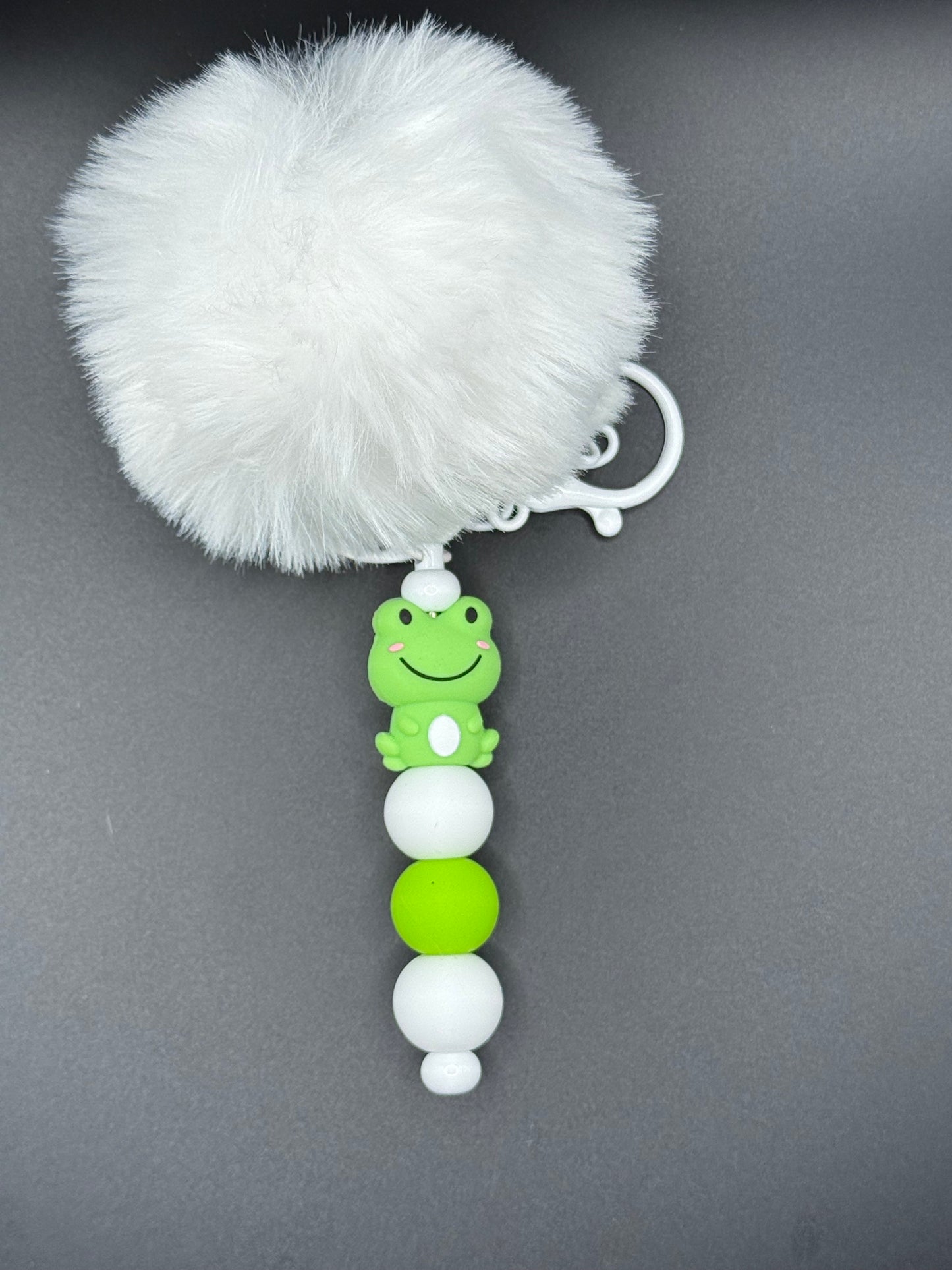 Keychain with white fluffy ball and green and white beads on a gray background