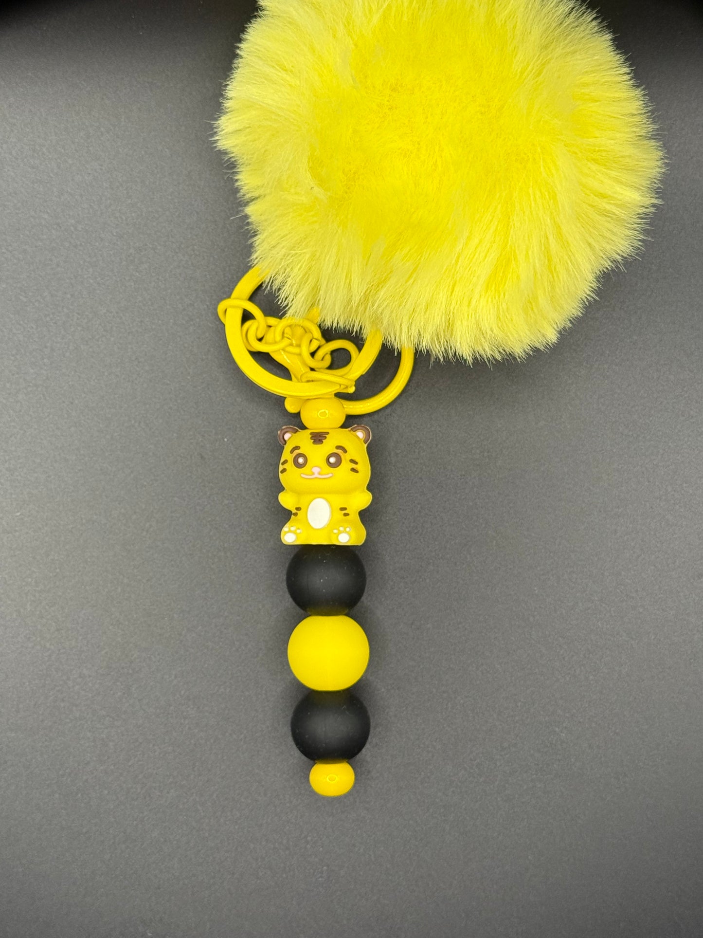 Yellow keychain with a fluffy attachment on a gray background