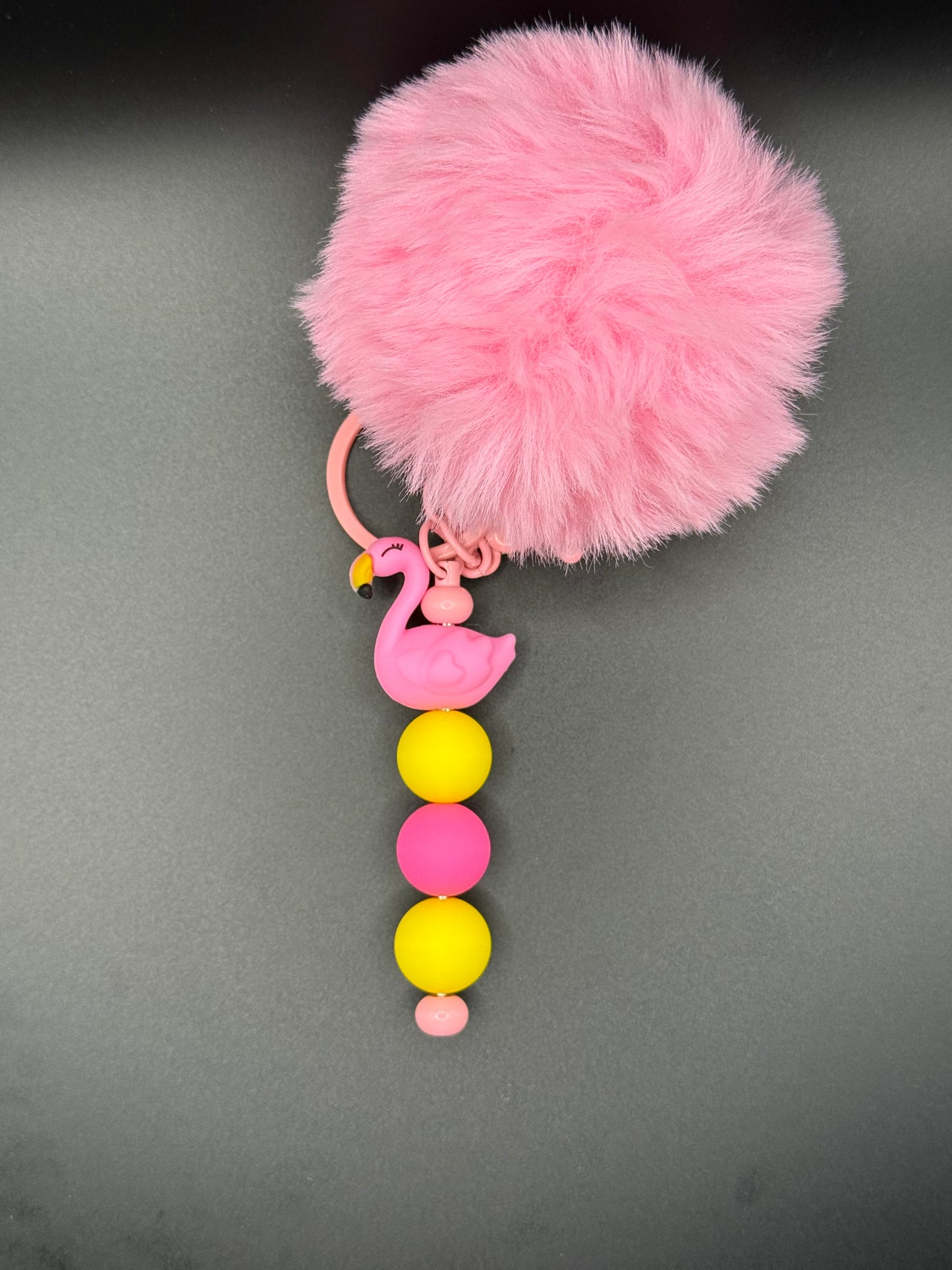 Pink fluffy keychain with colorful beads on a gray background