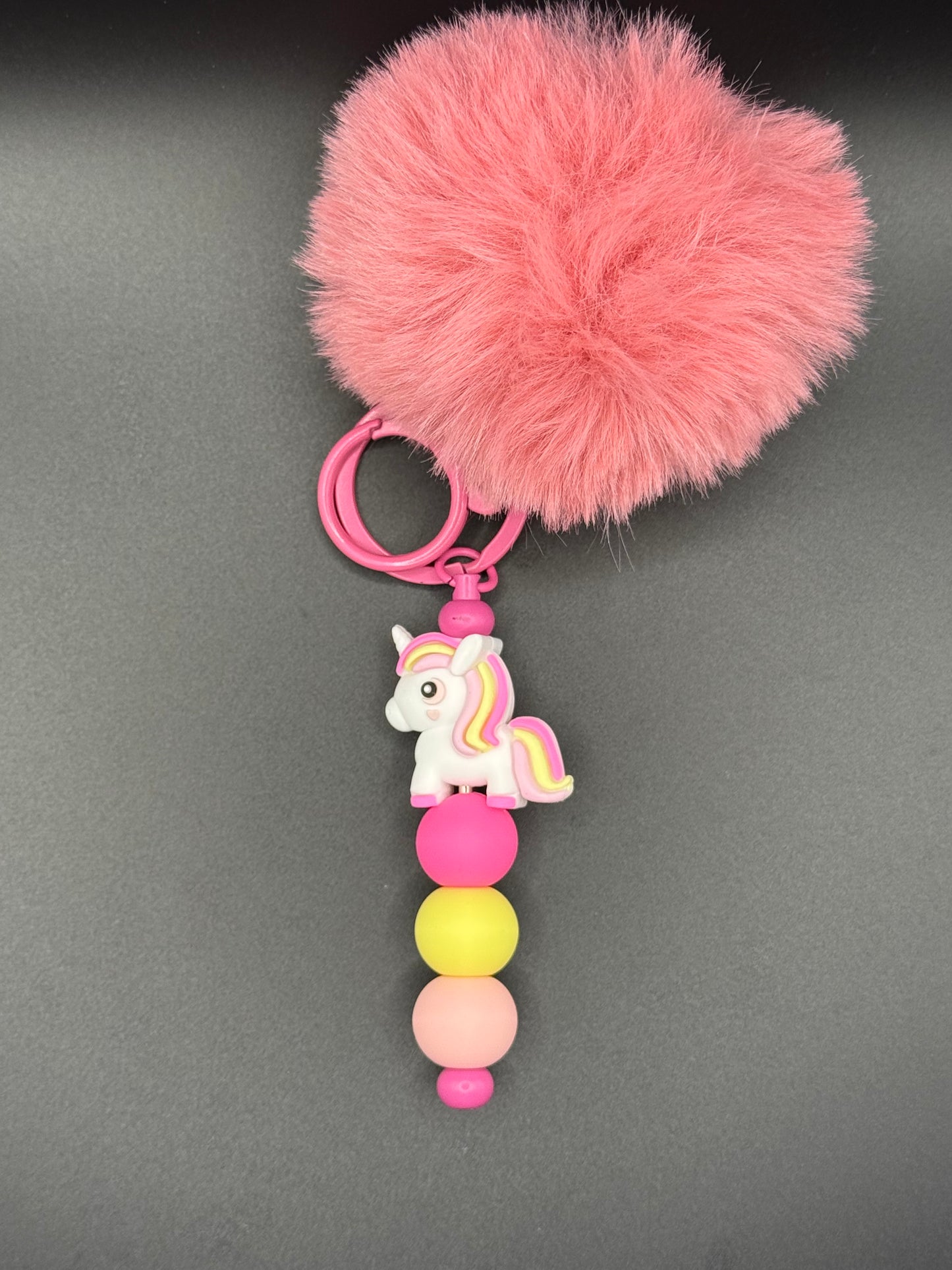 Pink fluffy pom-pom keychain with a unicorn charm on a gray background