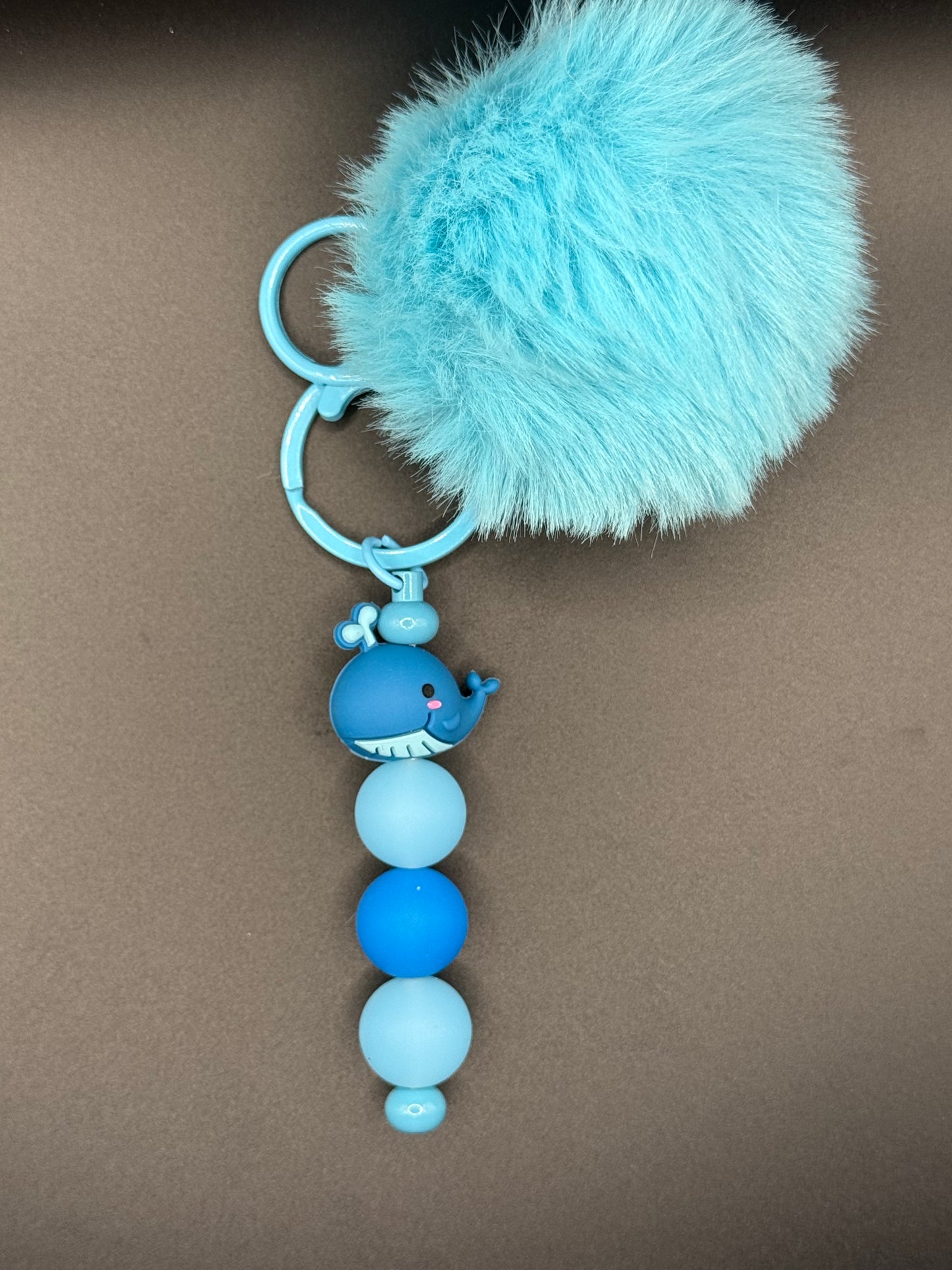 Blue keychain with a fluffy pom-pom and beaded chain on a brown background