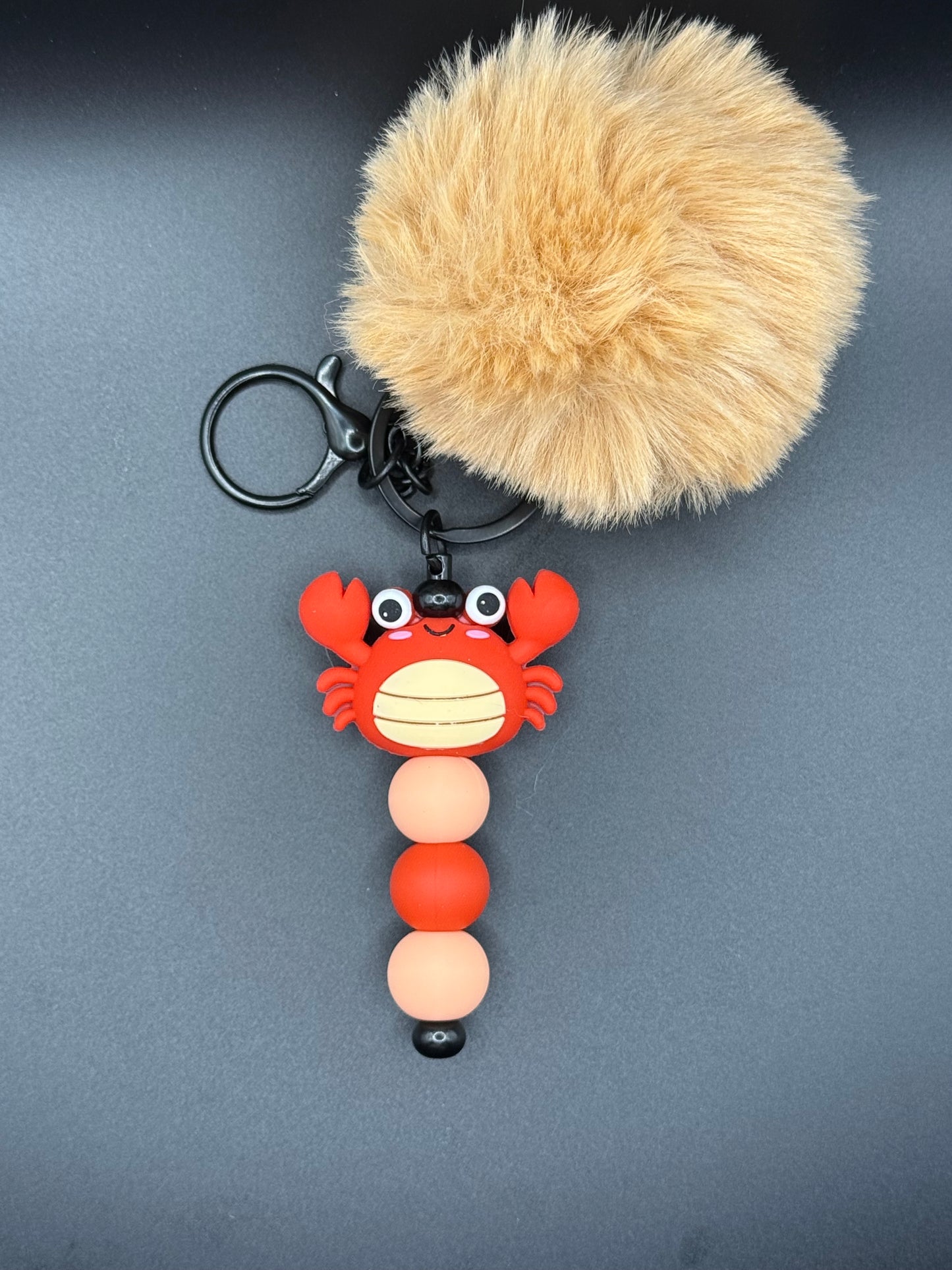 Keychain with fluffy ball and colorful lobster design on a gray background