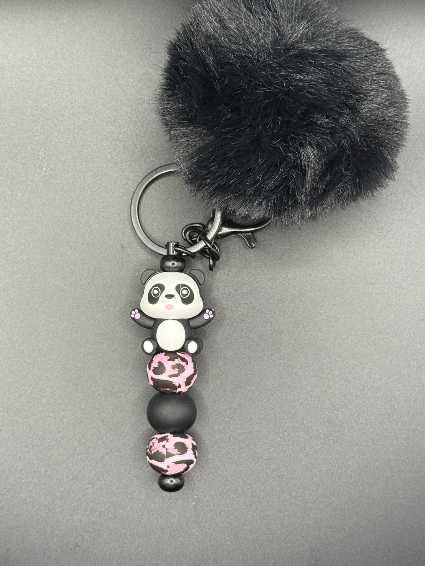 Keychain with black fur pom-pom and panda-shaped beads on a gray background