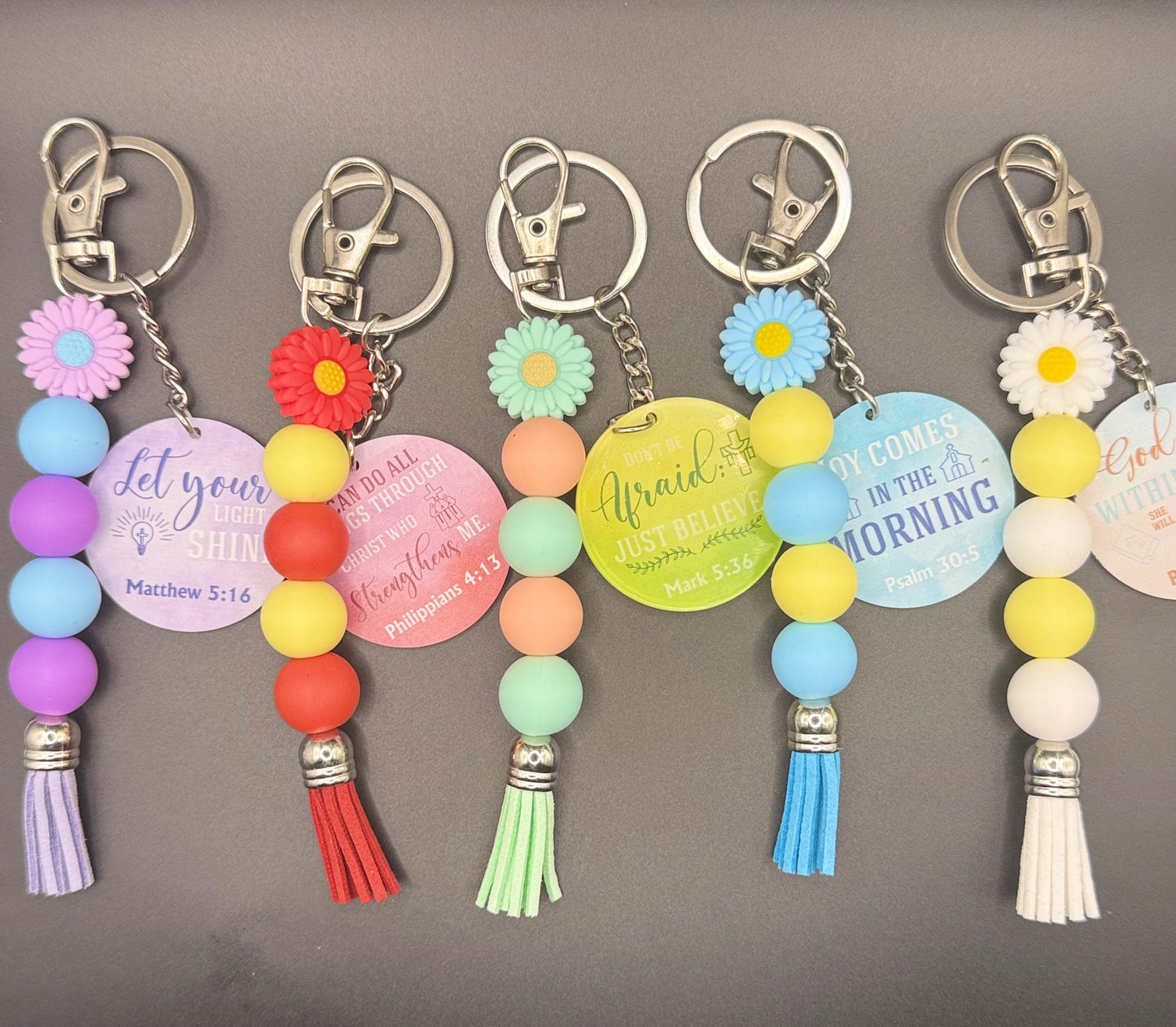 Colorful keychains with floral designs and motivational phrases on a gray background