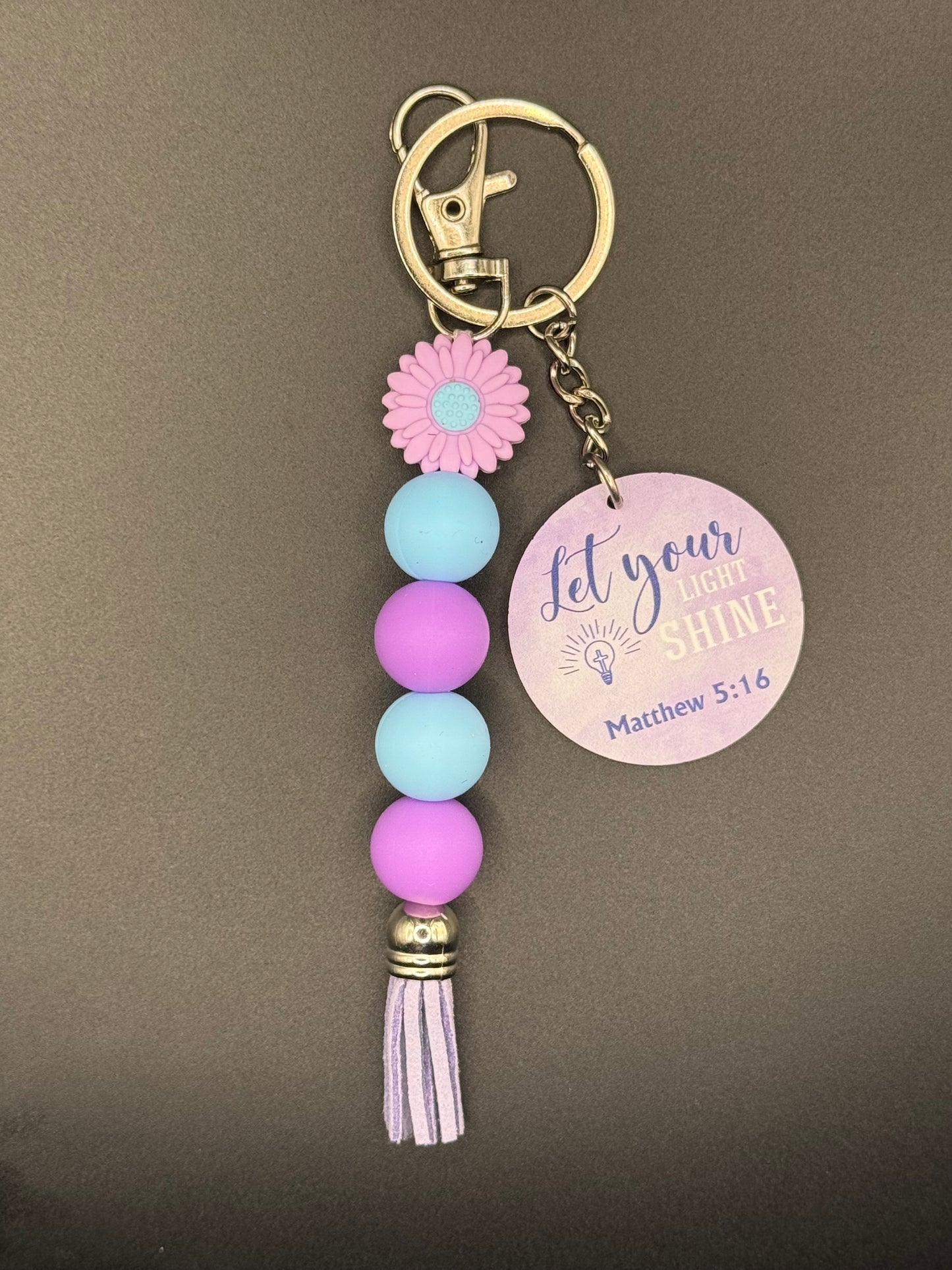 Purple Flower Keychain with colorful beads and a tassel on a gray background