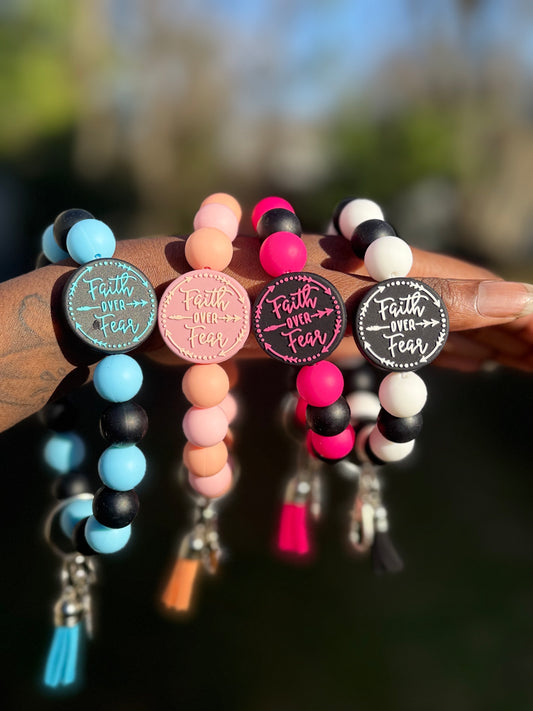 Colorful beaded bracelets with 'Faith Over Fear' charms held by a person.