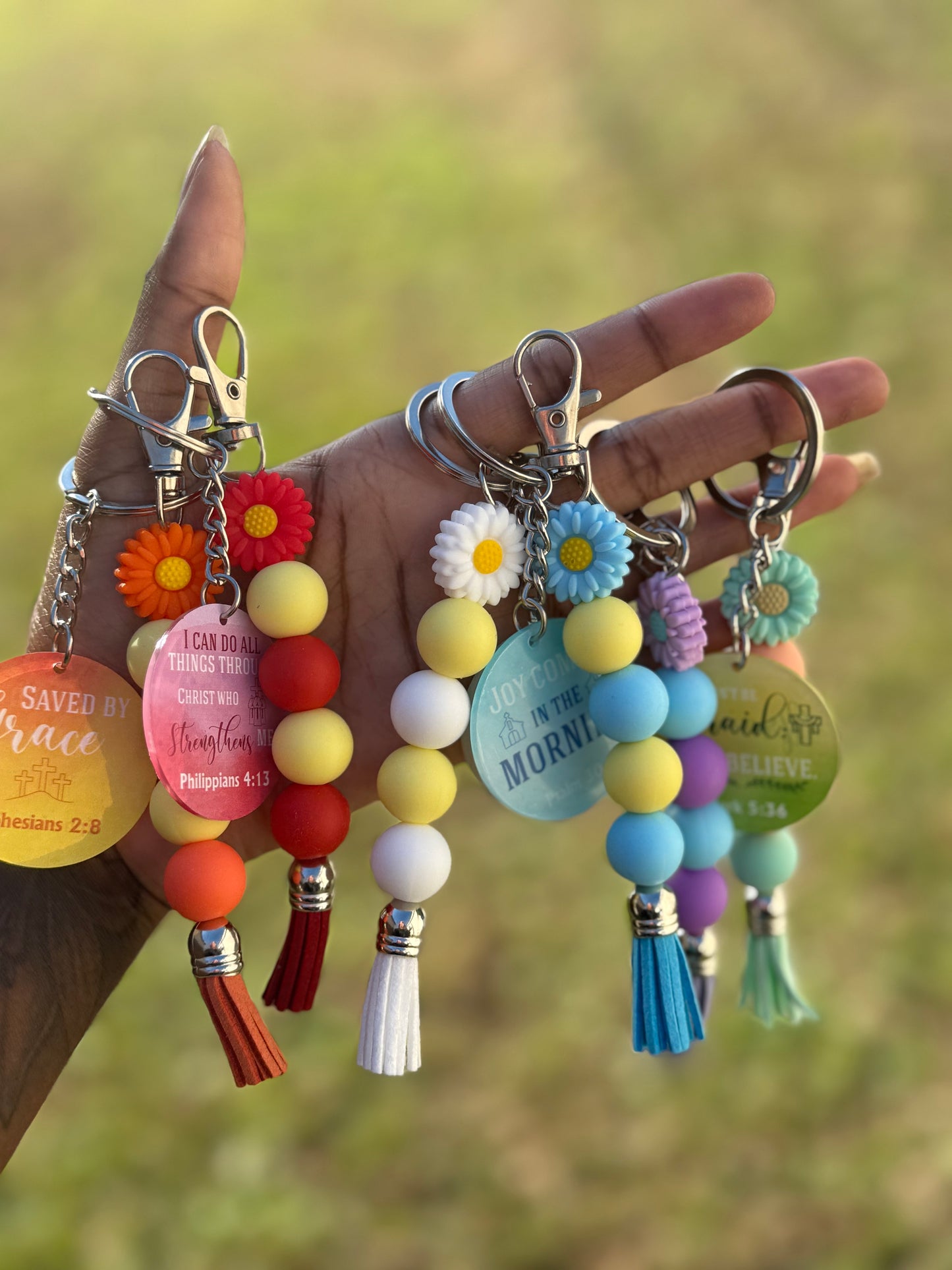 Colorful keychains with beads and charms held by a hand against a blurred natural background