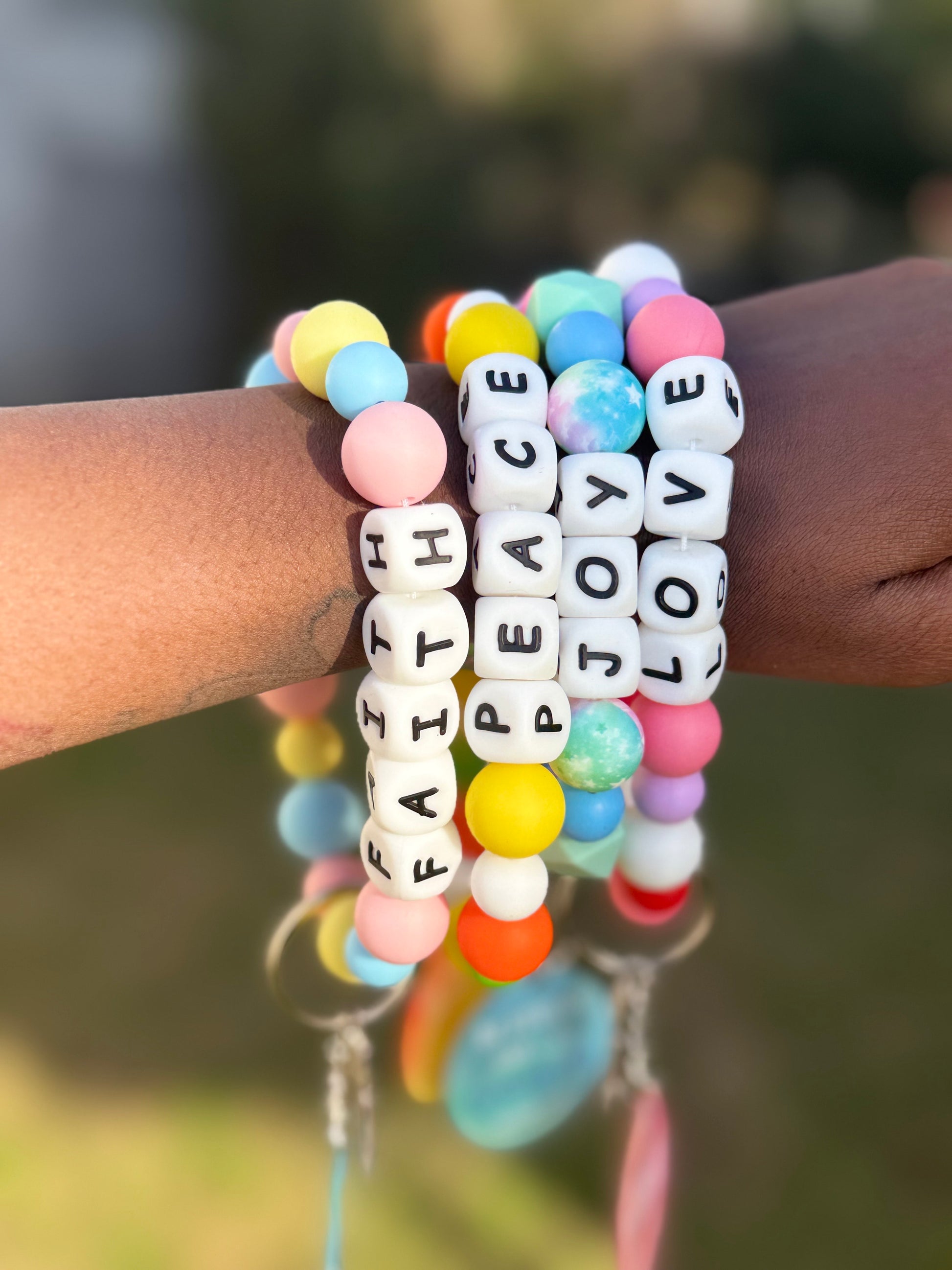 Colorful beaded bracelets with motivational words on a wrist against a blurred natural background