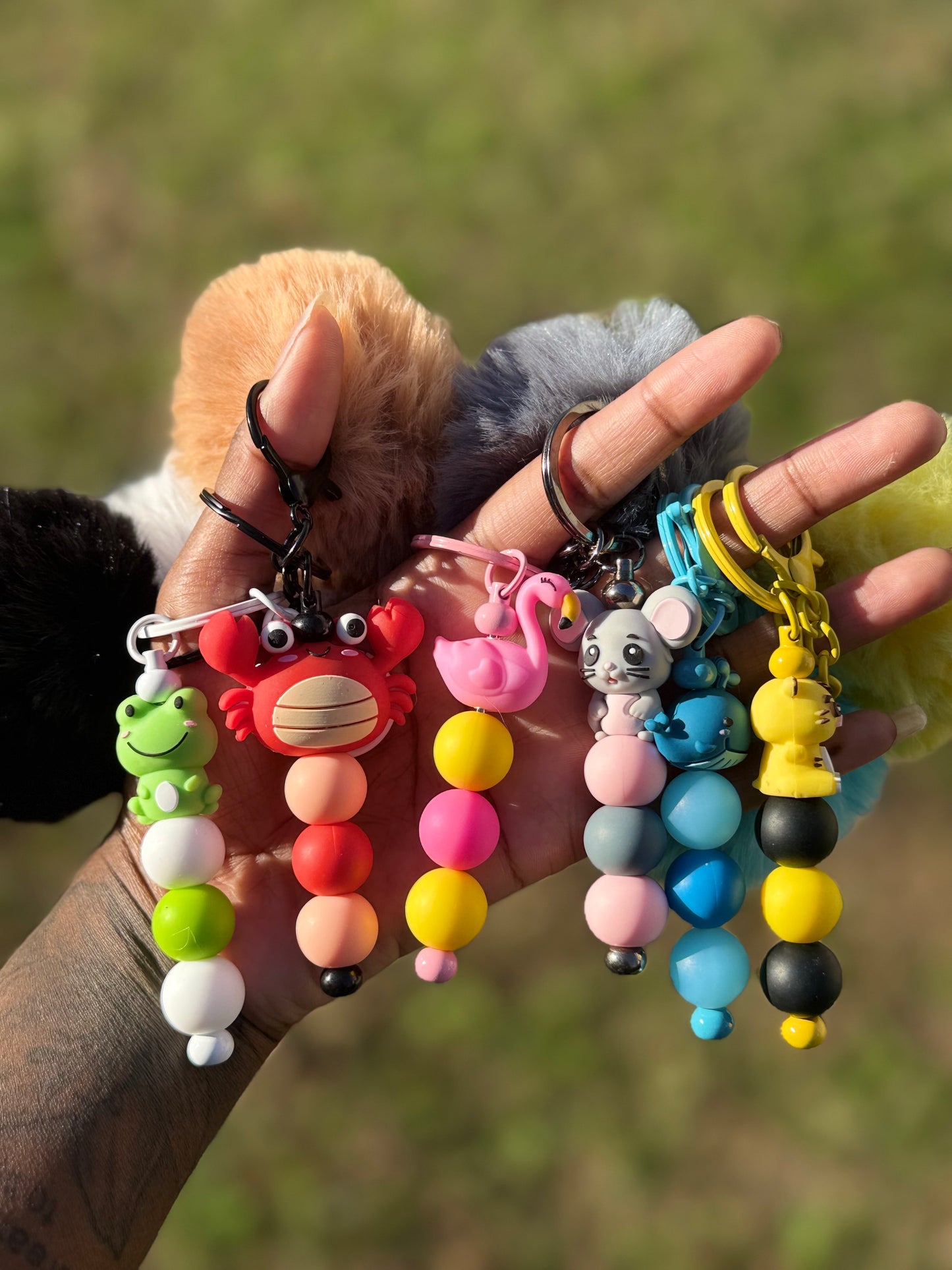 Colorful keychains with animal figures held in a hand against a blurred natural background