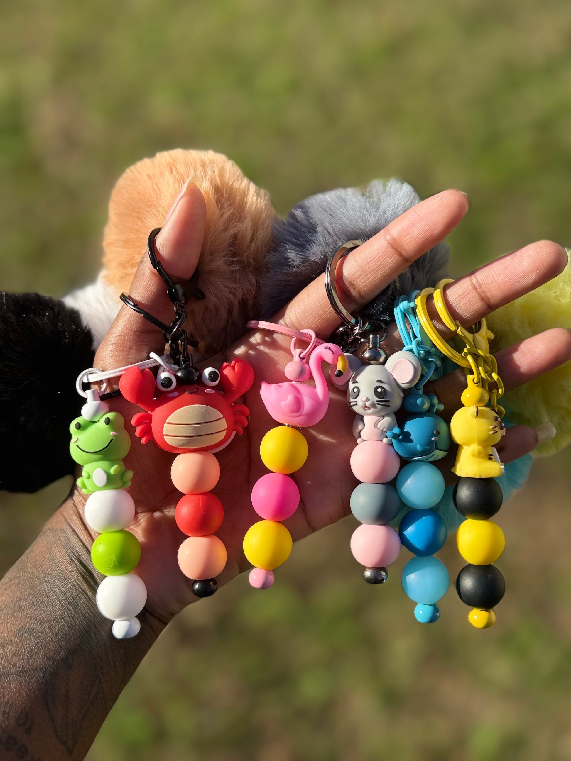 Colorful keychains with animal figures held in a hand against a blurred natural background