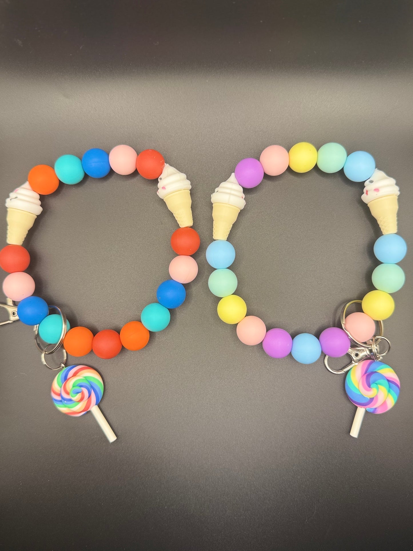 Two colorful bracelets with ice cream and lollipop charms on a gray background