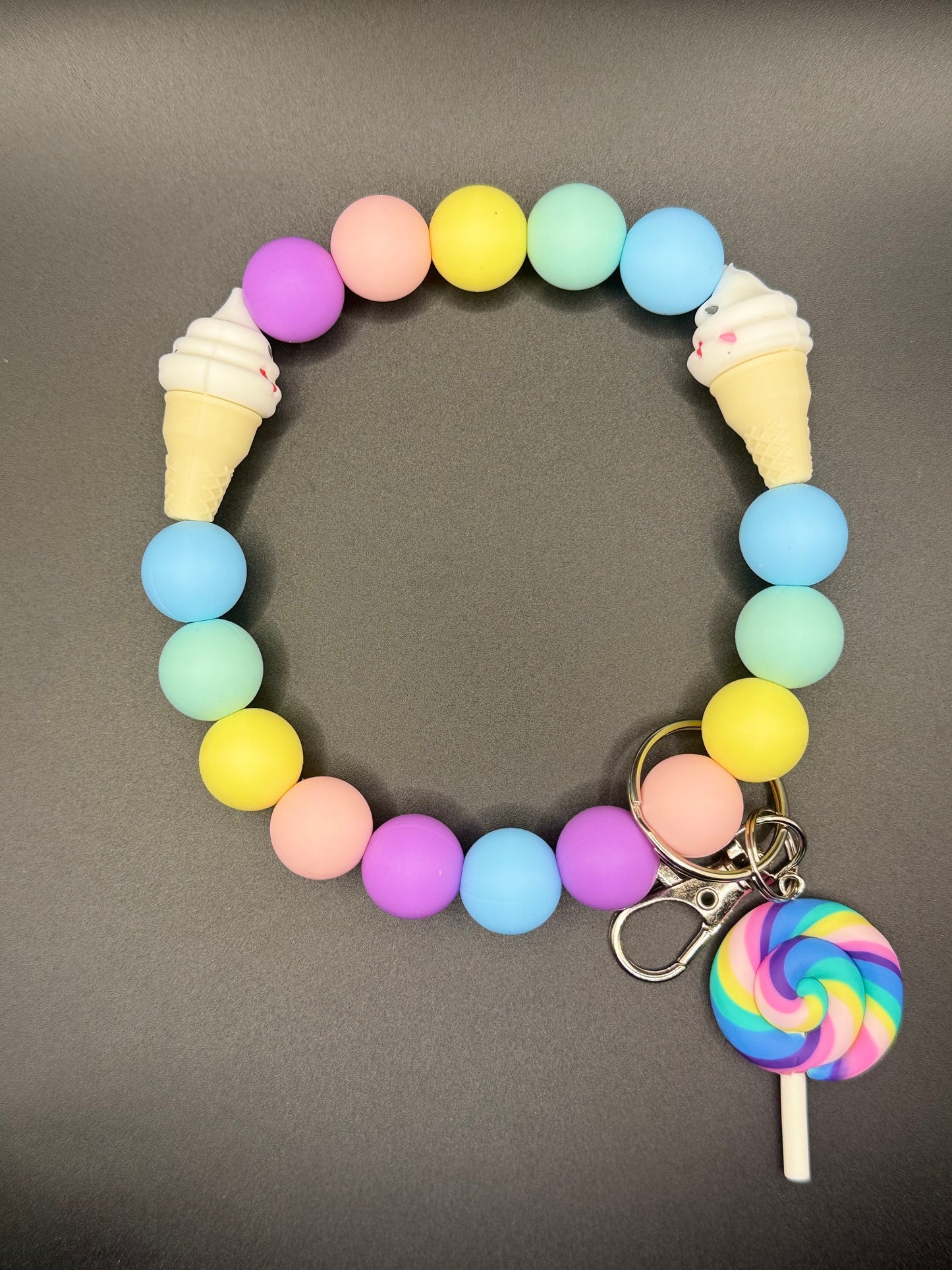 Colorful beaded bracelet with ice cream and lollipop charms on a gray background