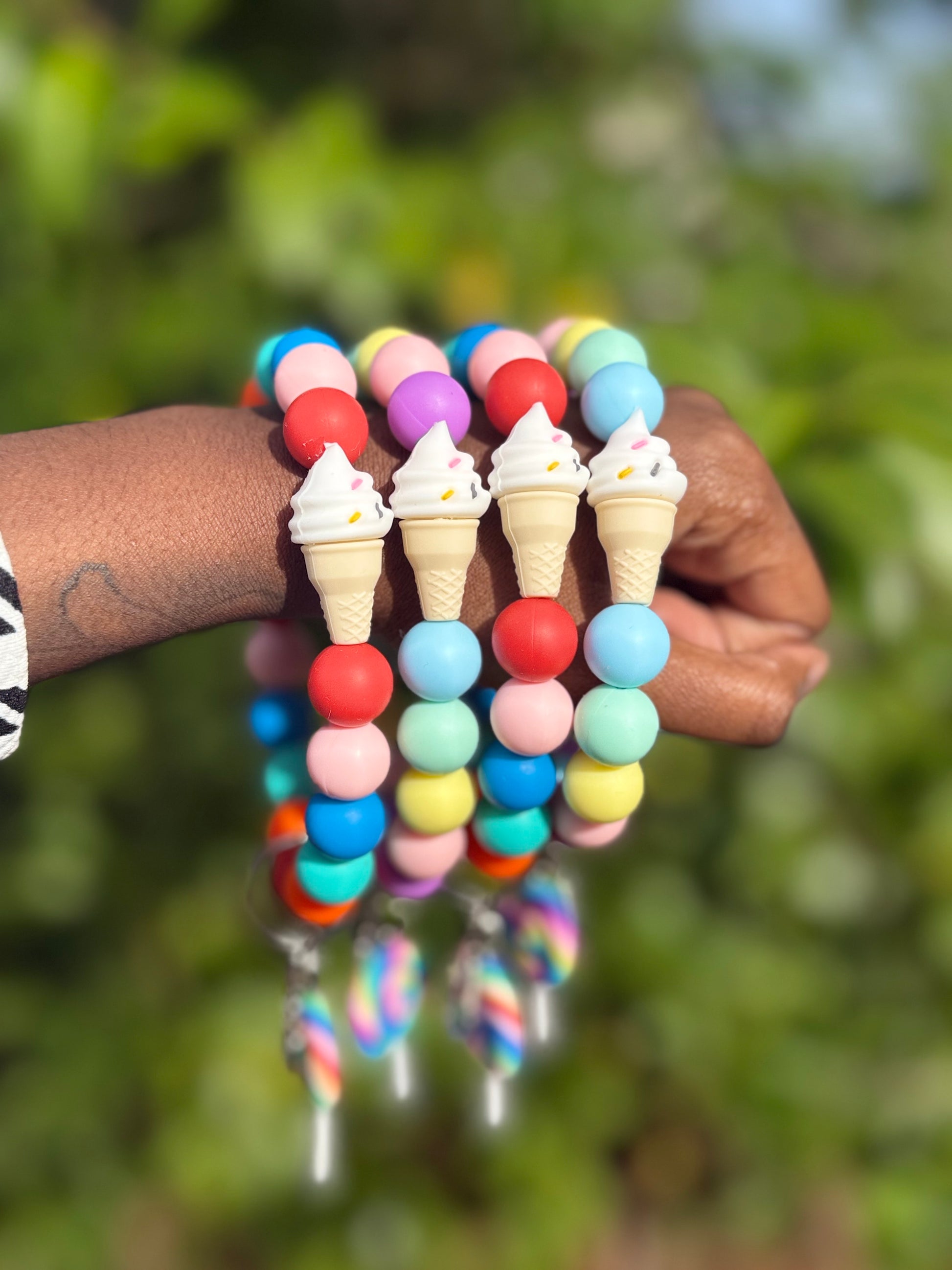 Colorful beaded bracelet with ice cream cone and waffle designs held by a person against a blurred green background.