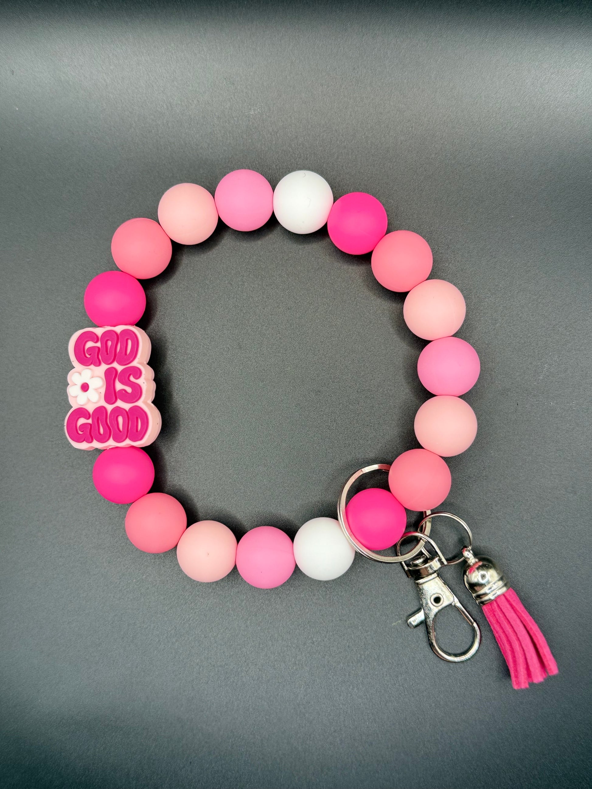 Pink beaded bracelet with 'God is Good' charm on a gray background
