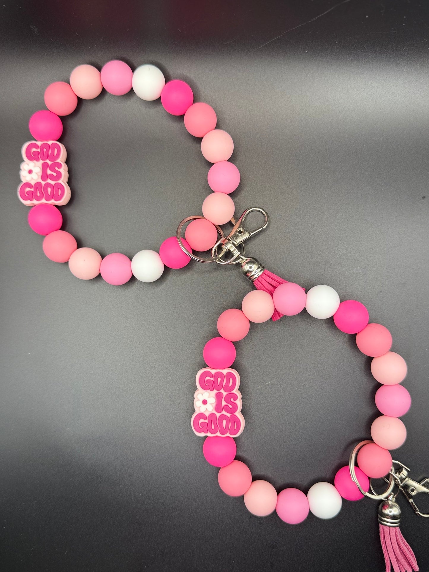 Pink and white beaded bracelet with 'GOD IS GOOD' charm on a gray background