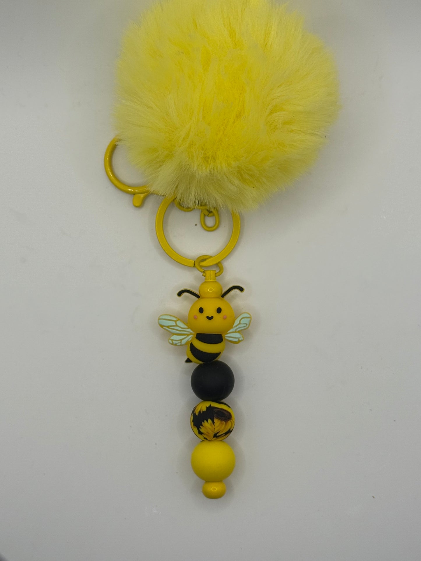 Yellow pom-pom keychain with a bee-shaped charm on a white background