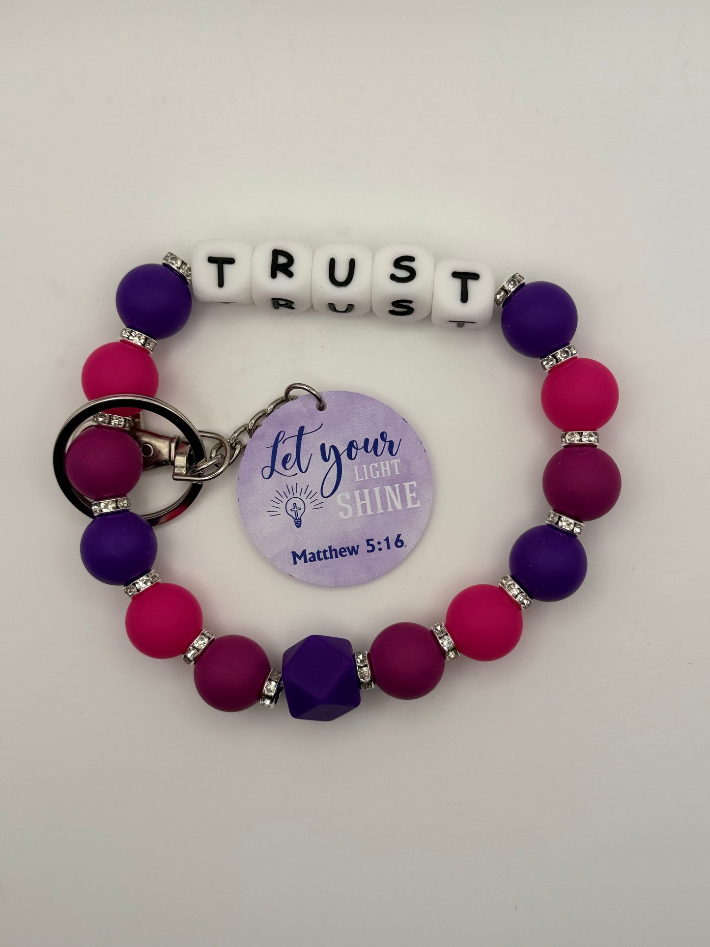 Bracelet with letter beads spelling 'TRUST' and a keychain on a white background 