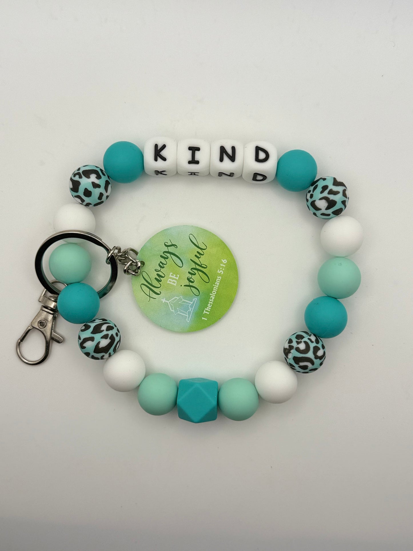 Bracelet with turquoise and white beads with letter beads spelling 'KIND 'and a keychain on a light gray background