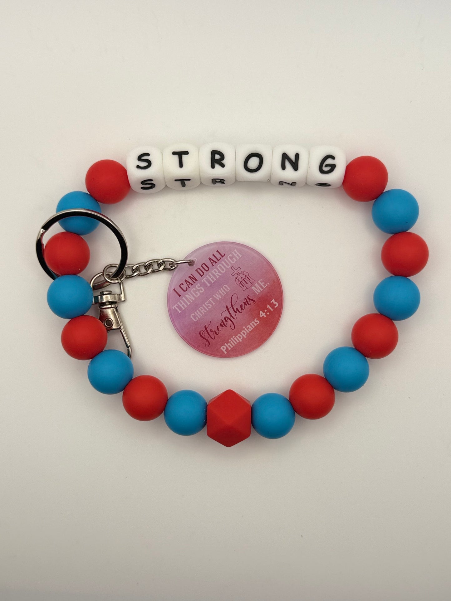 Bracelet with red and blue beads with letter beads spelling 'STRONG' and a keychain on a white background