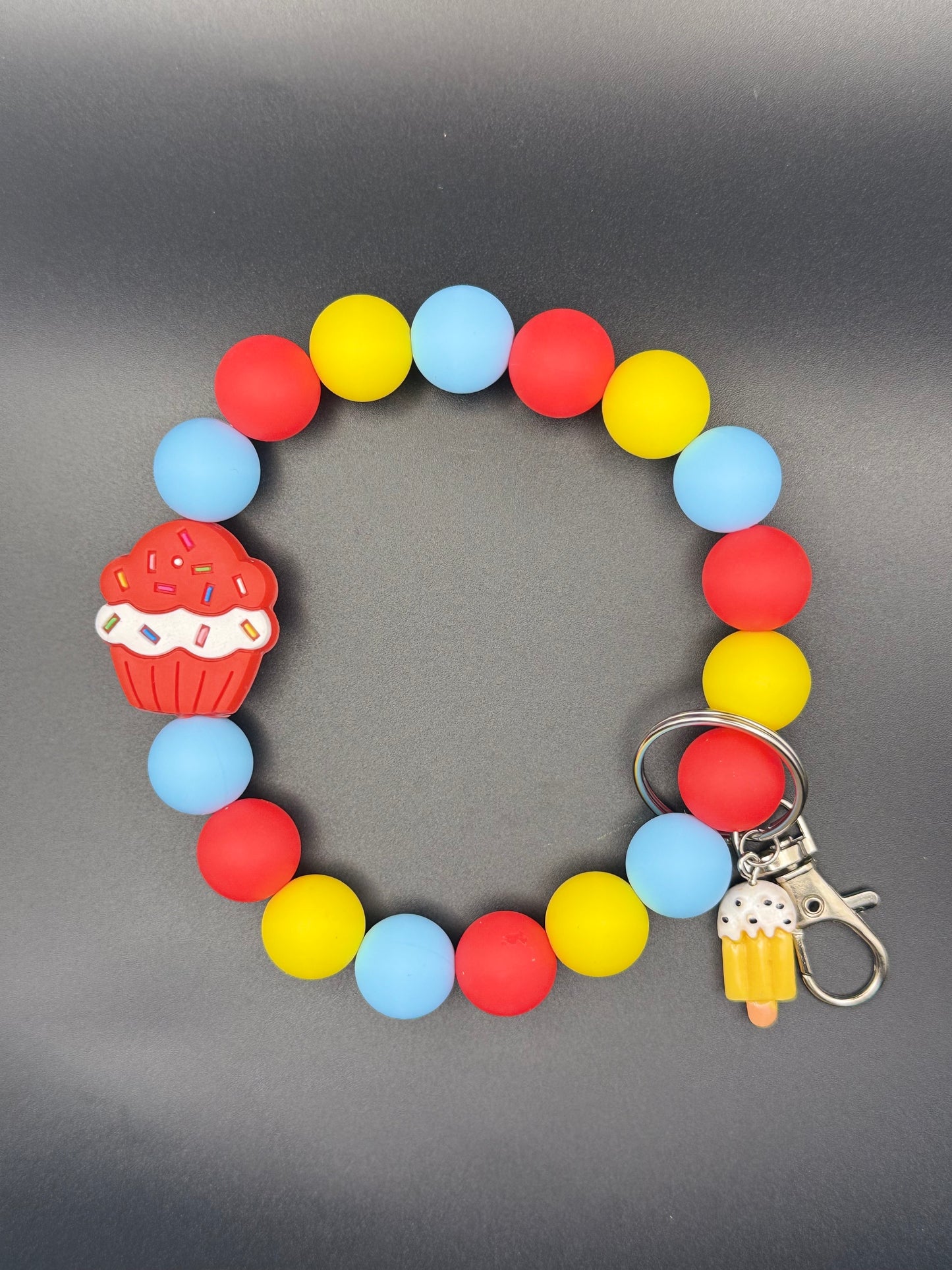 Colorful beaded bracelet with cupcake and ice cream keychain on a gray background