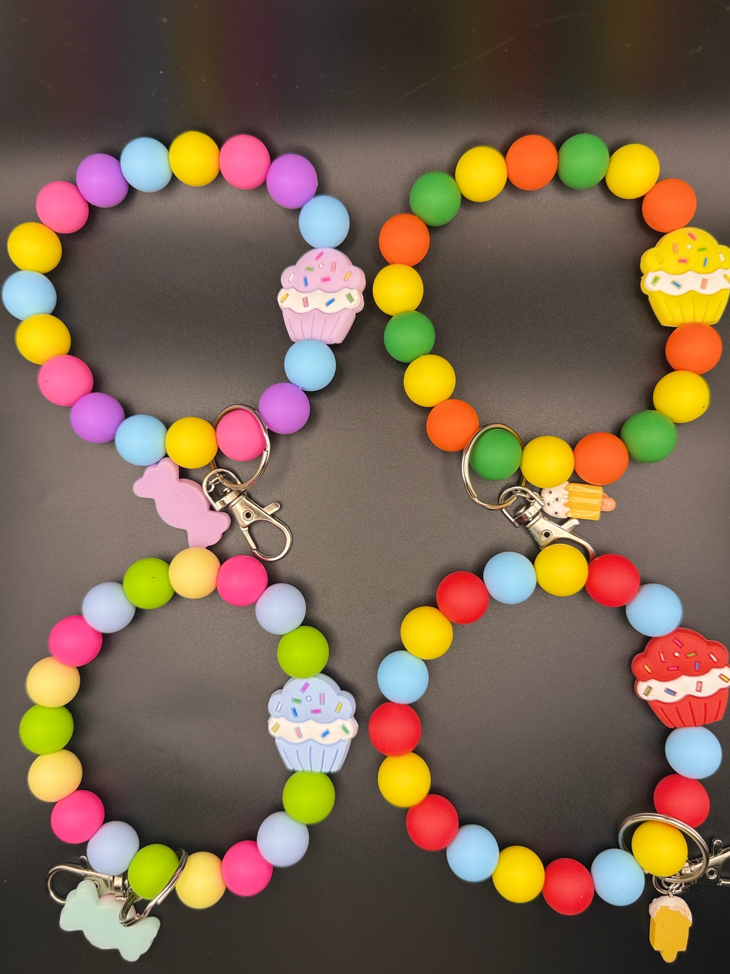 Two colorful keychains with bead designs and cupcake charms on a dark background.