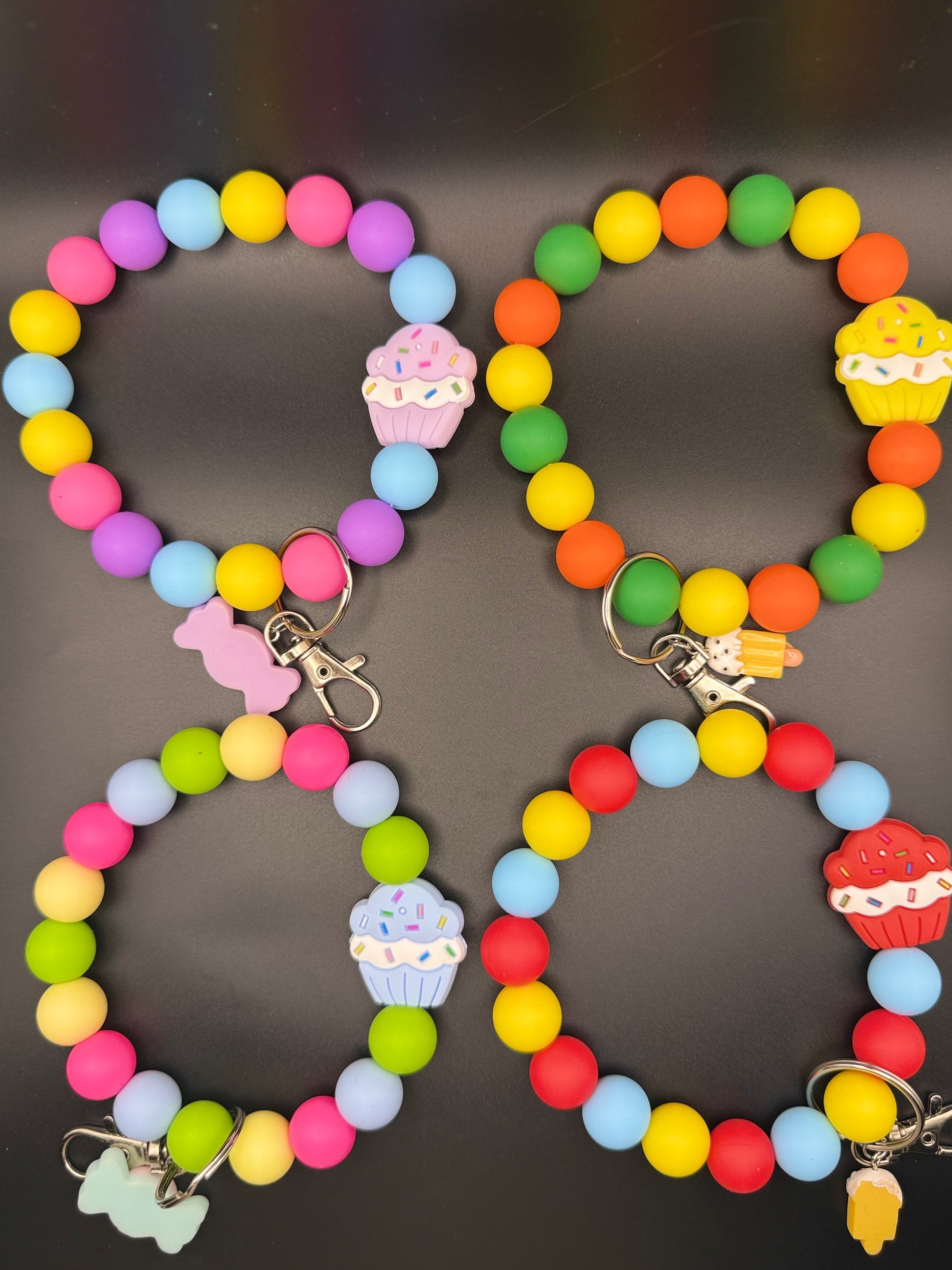 Two colorful keychains with bead designs and cupcake charms on a dark background.
