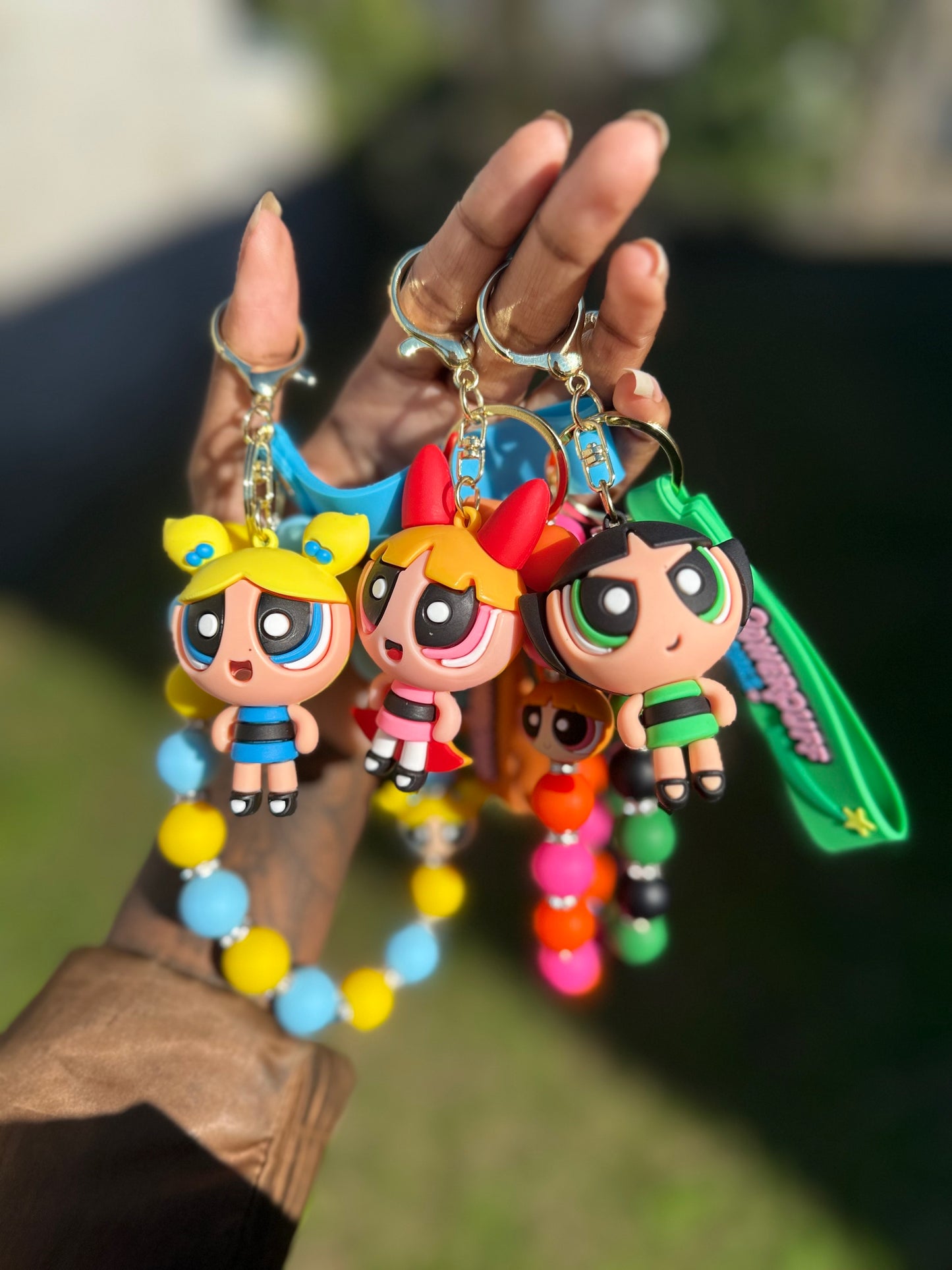Colorful keychains shaped like cartoon characters held by a hand against a blurred background.