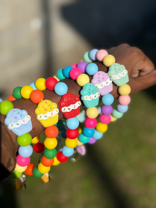 Colorful beaded bracelets with cupcake charms on a blurred background