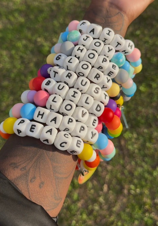 Colorful beaded bracelet with motivational words held by a person against a blurred green background