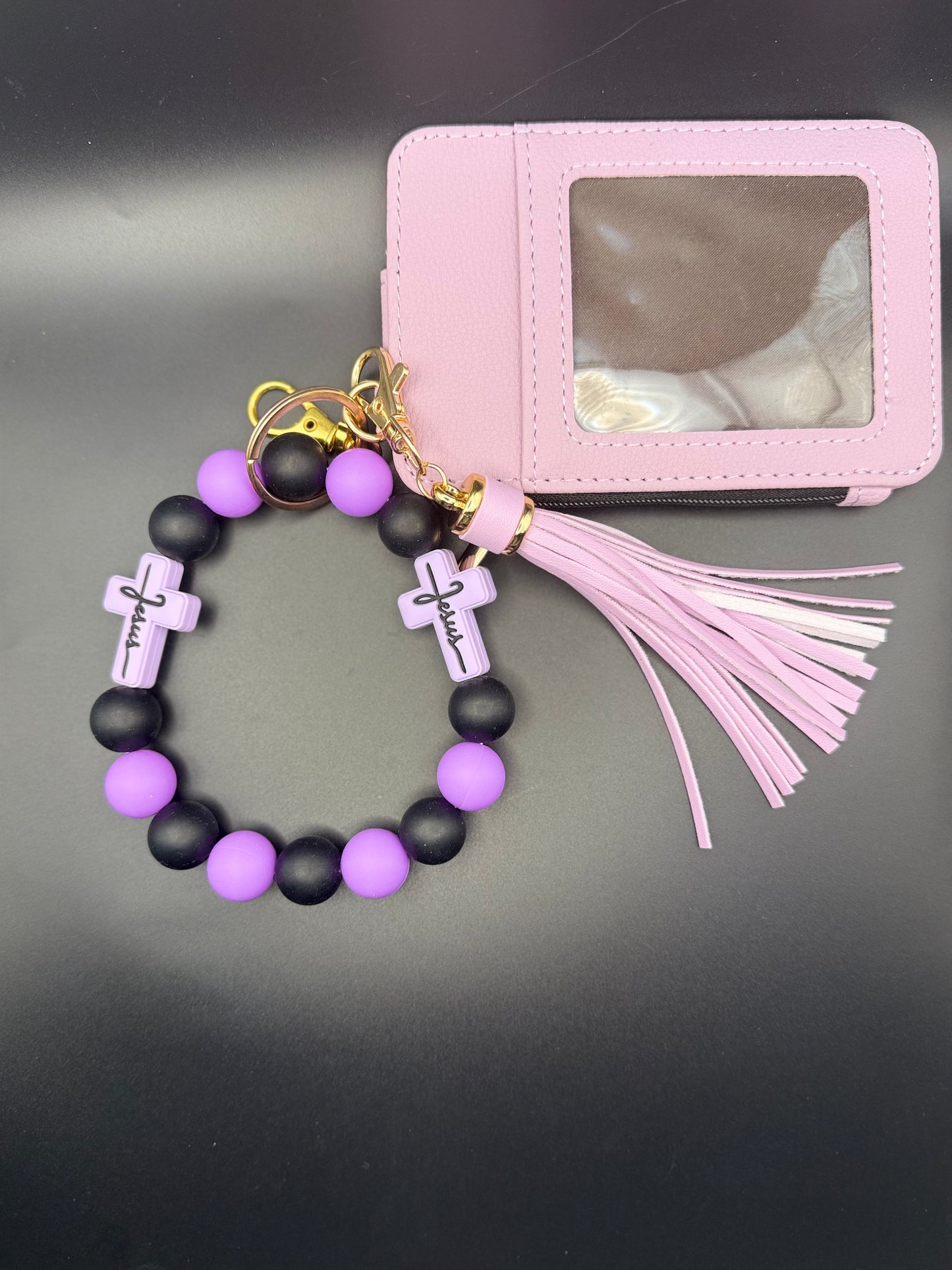 Bracelet with black and purple beads and 'Jesus' charms, attached to a pink keychain with tassel on a dark background.