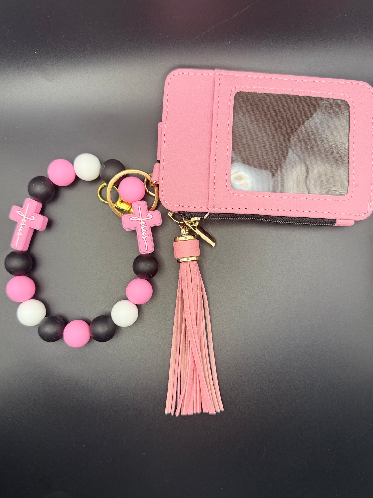 Pink bracelet with cross charms and tassel next to a pink cardholder on a dark surface