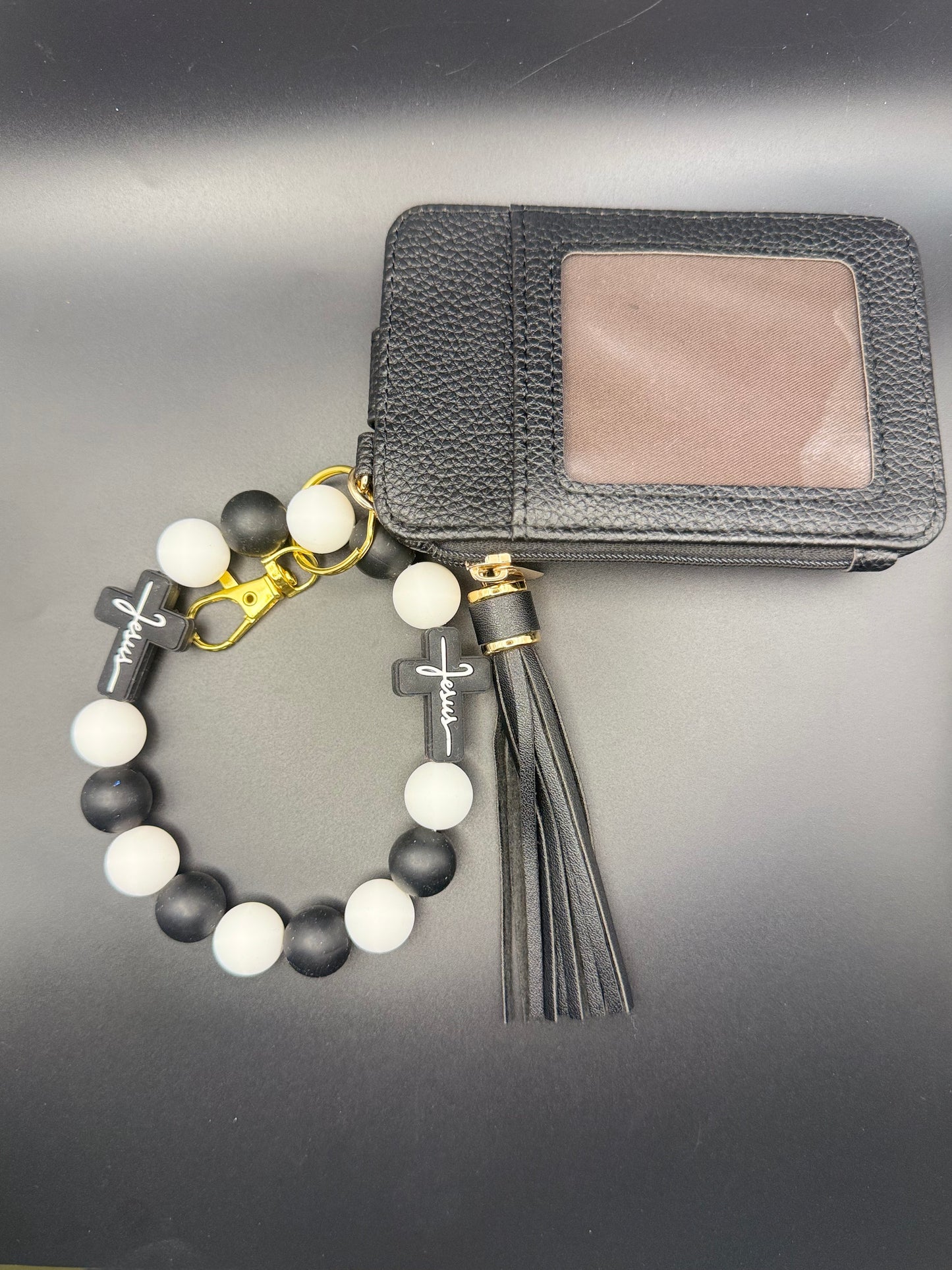 Black and white beaded bracelet with tassel next to a black wallet on a gray surface