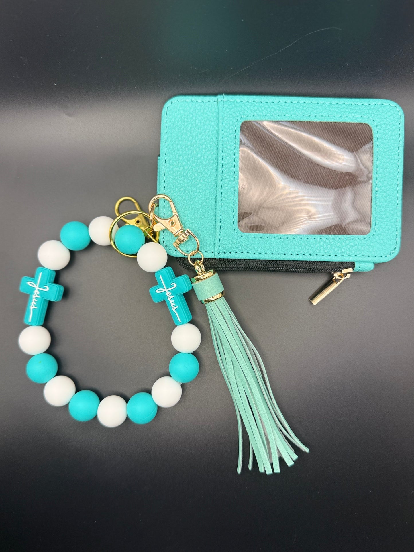 Turquoise beaded bracelet with tassel and cross charm next to a turquoise cardholder on a dark background