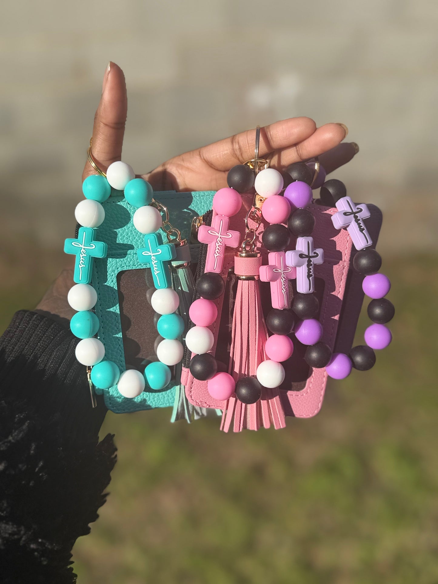 Three colorful keychains with beads and crosses held by a hand against a blurred natural background.