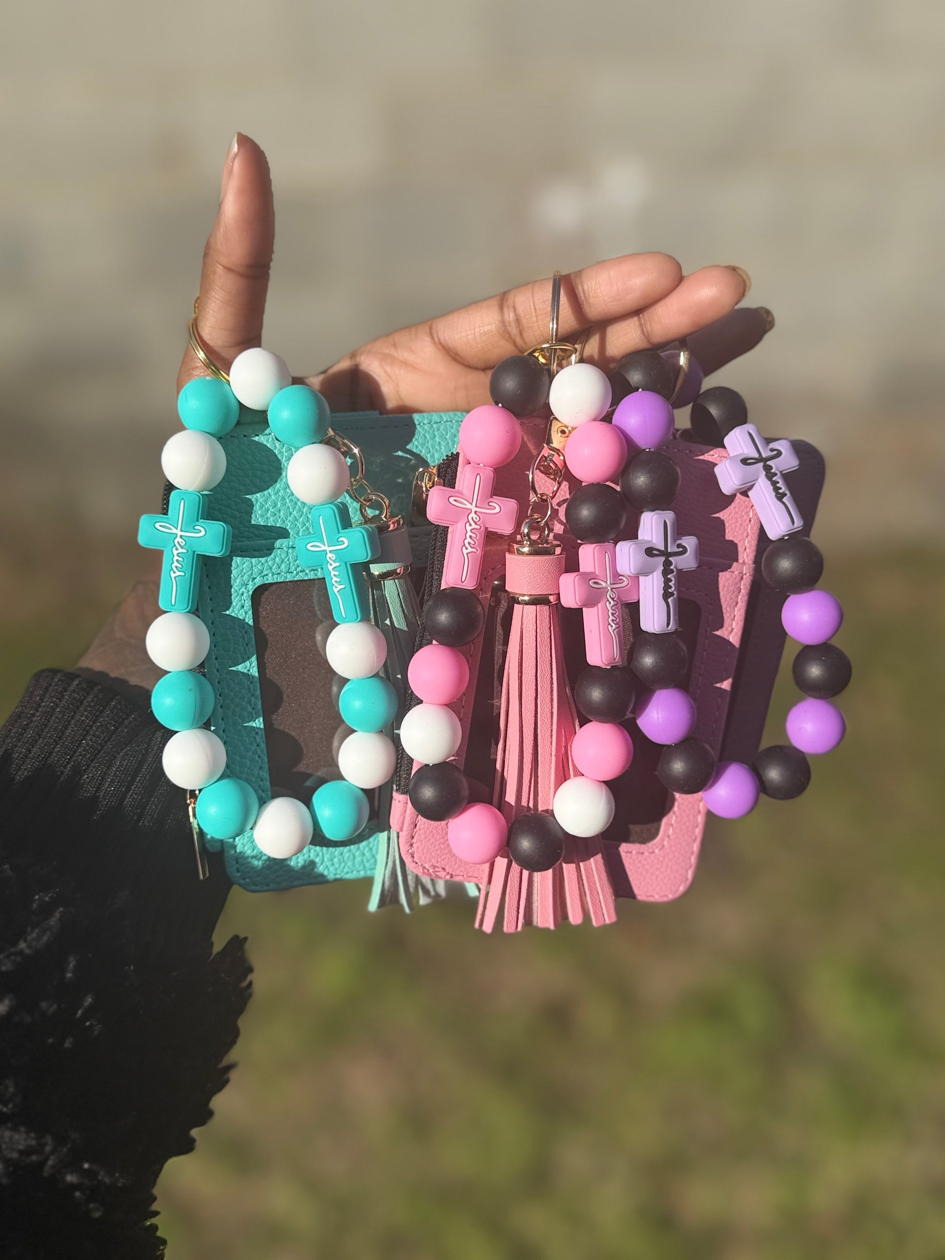Three colorful keychains with beads and crosses held by a hand against a blurred natural background.