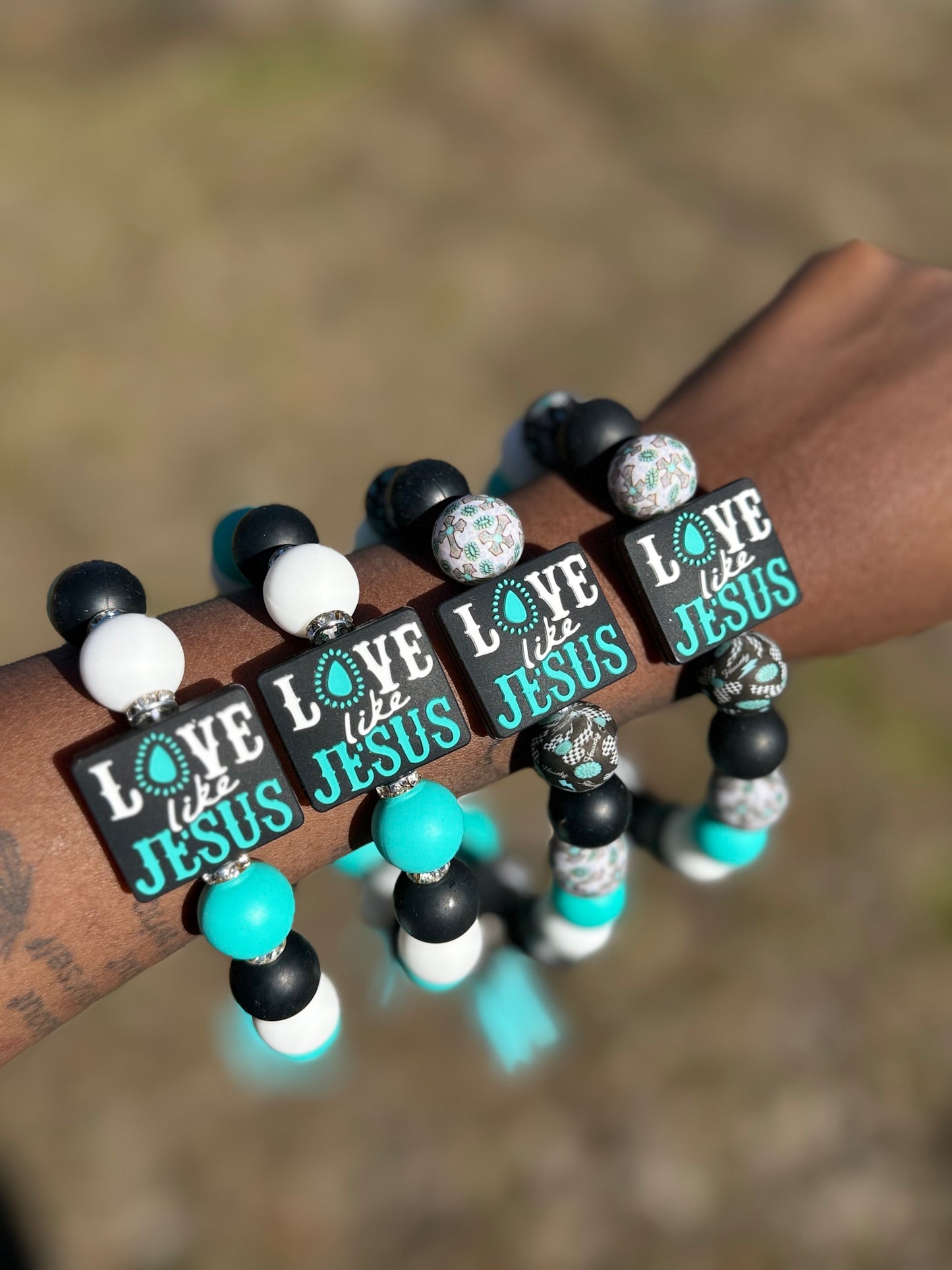 Bracelets with 'Love like Jesus' text on a wrist against a blurred background