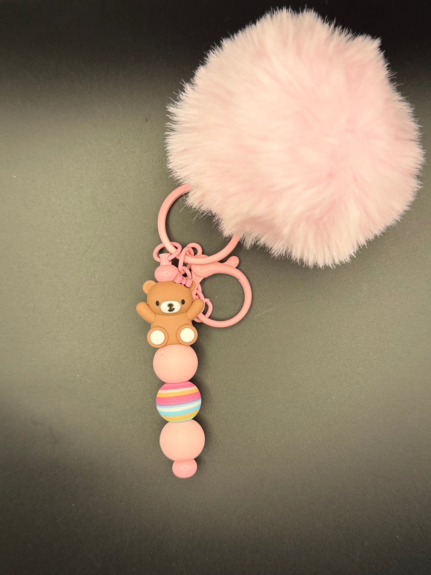 Pink fluffy keychain with a teddy bear charm on a dark background
