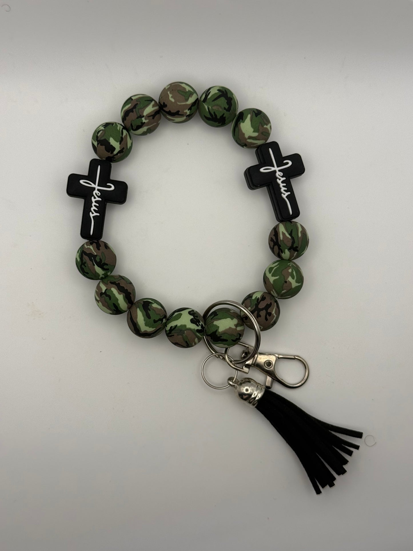 Camouflage beaded bracelet with 'Jesus' crosses and a black tassel on a light gray background