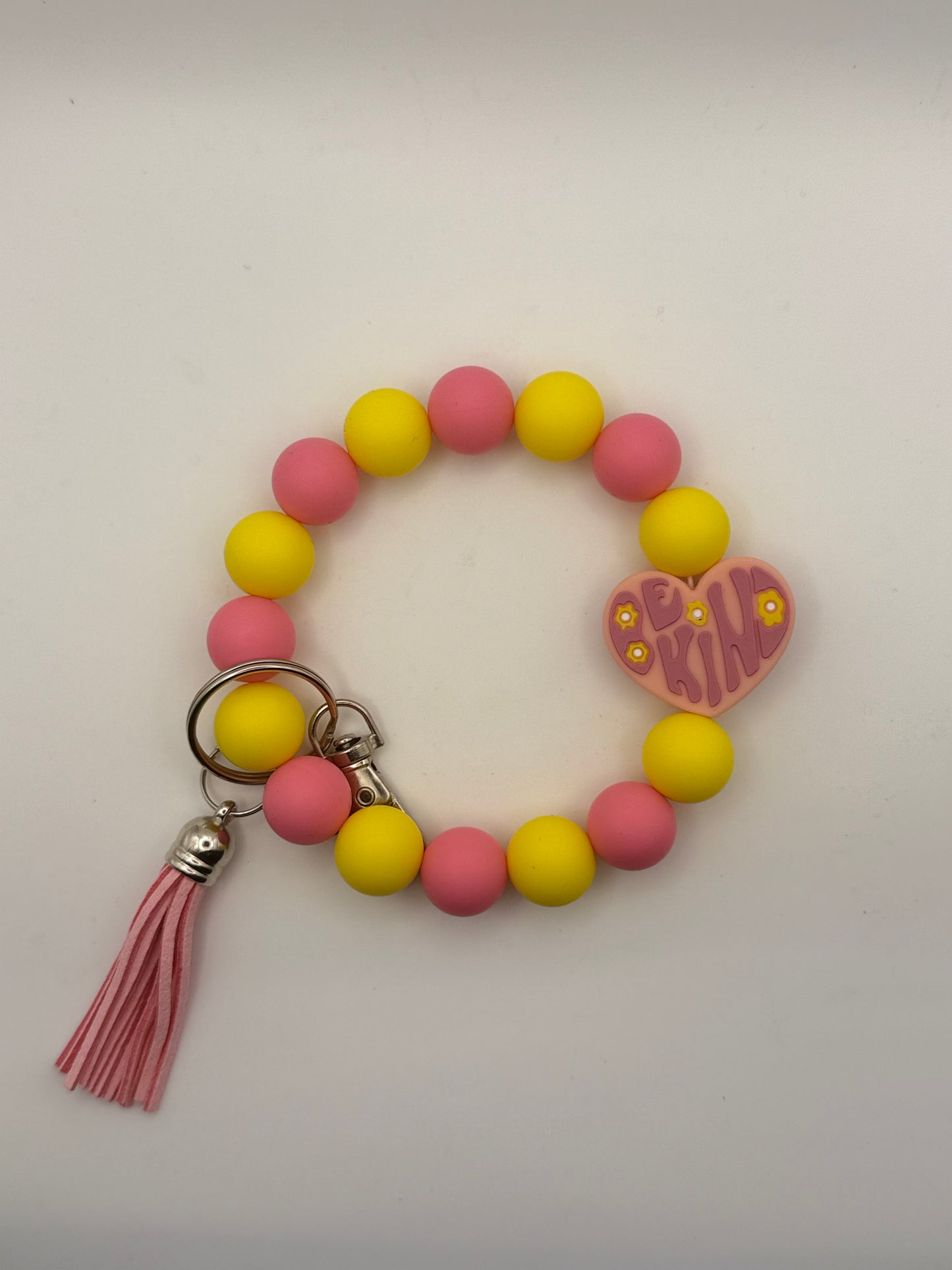 Bracelet with pink and yellow beads, tassel, and heart-shaped charm on a light gray background