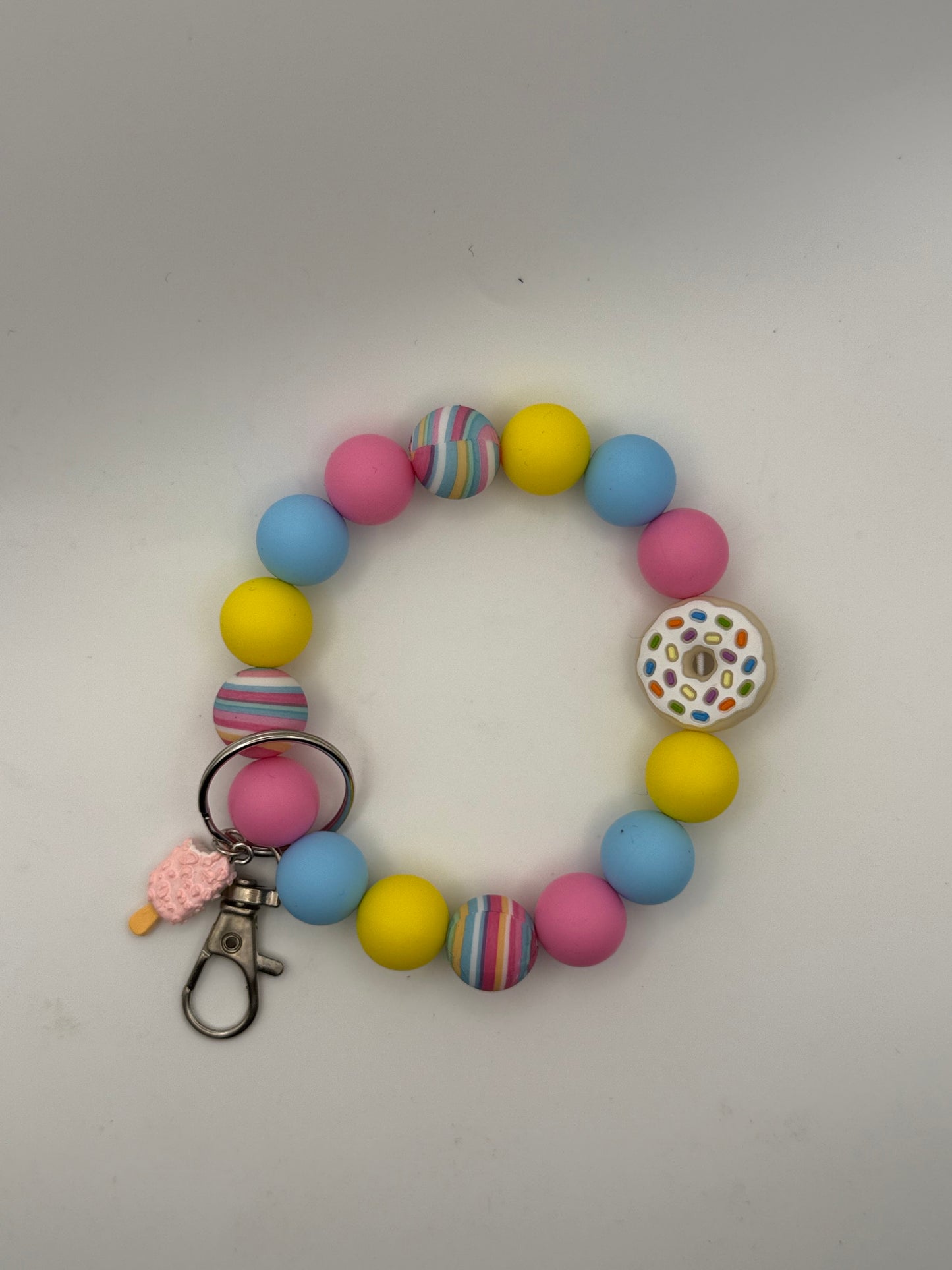 Colorful beaded bracelet keychain with donut charm on a light gray background