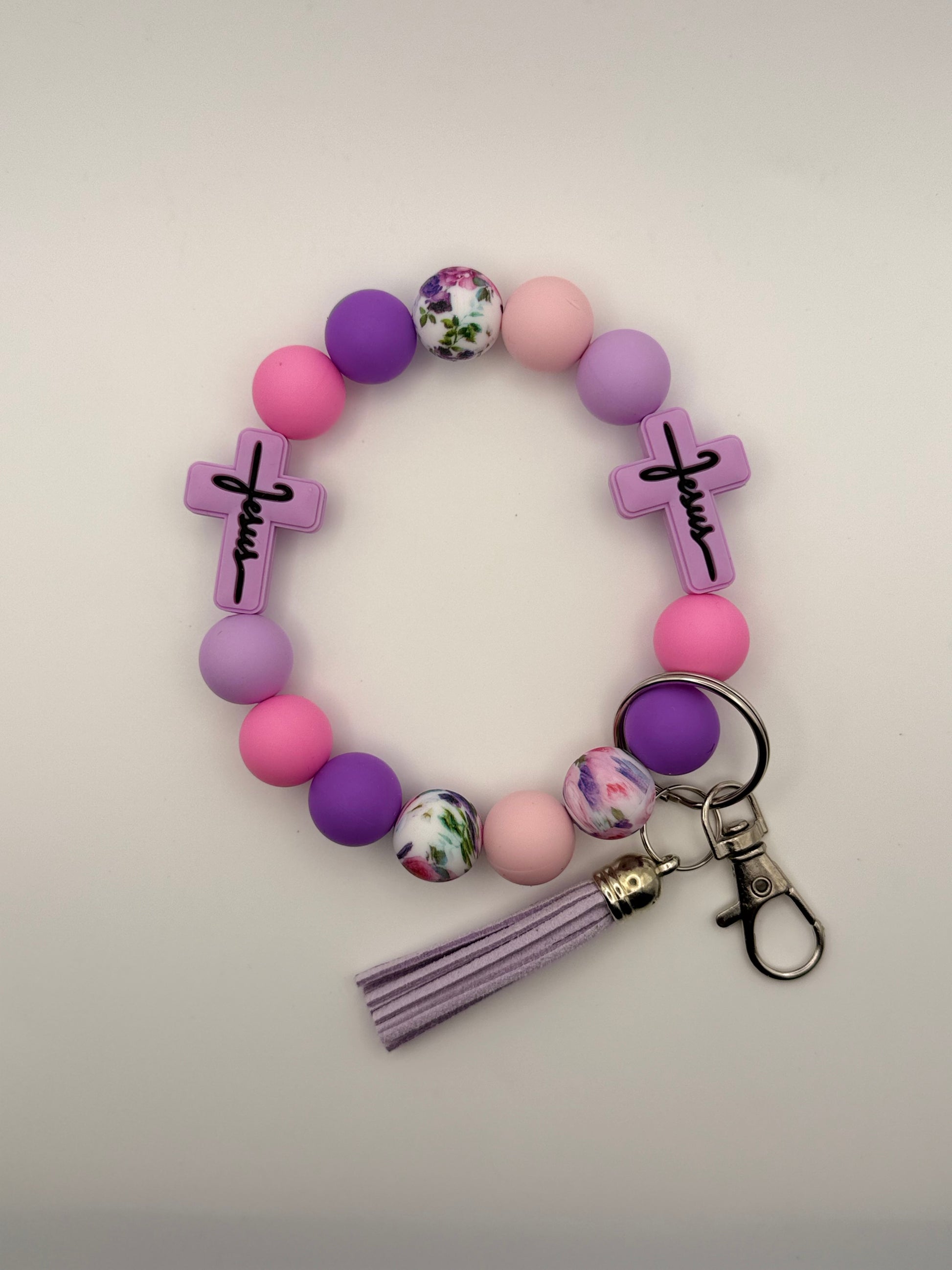 Purple beaded keychain with floral charm and tassel on a light gray background