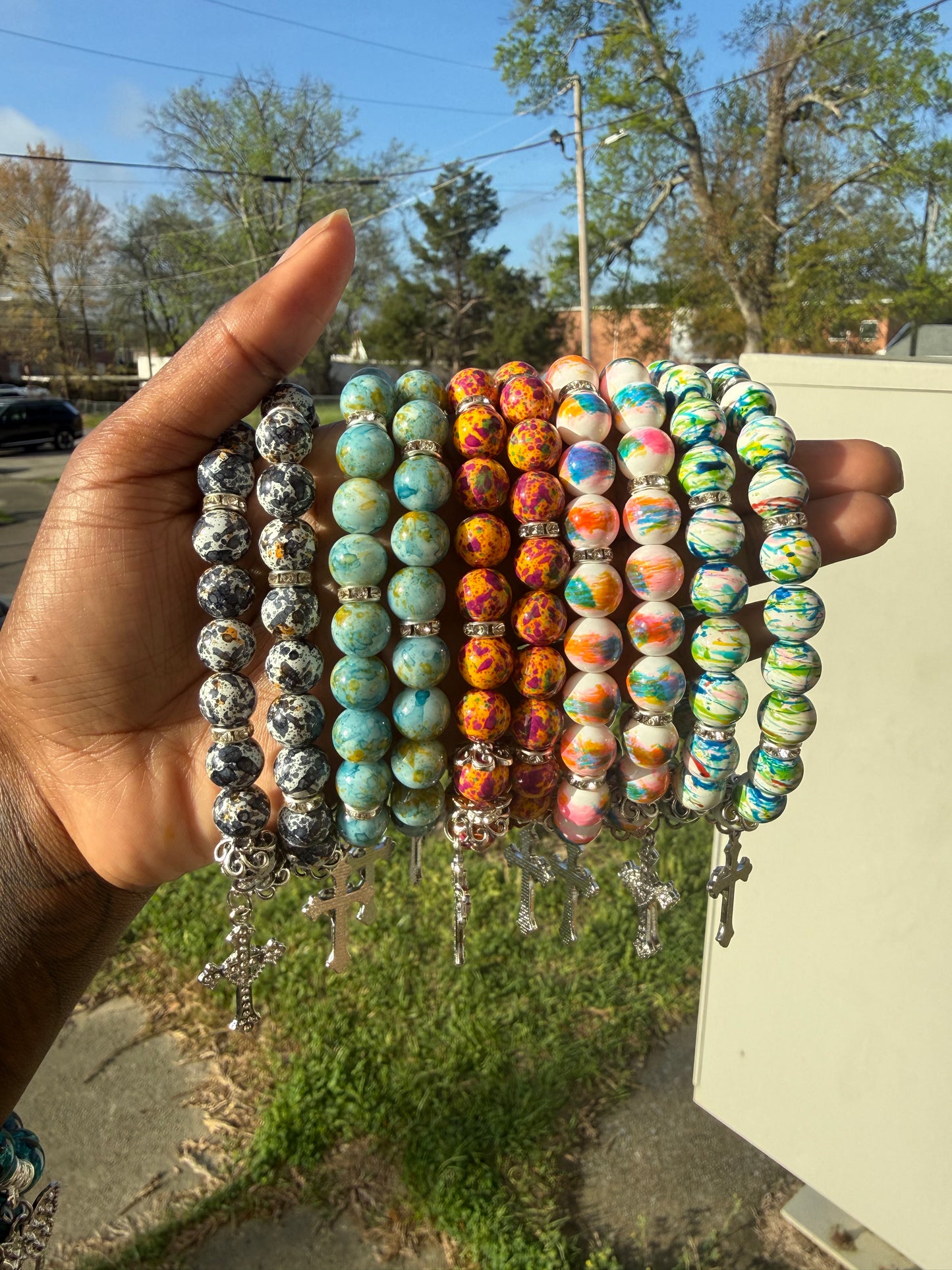 Stack of colorful beaded bracelets held by a hand with a blurred outdoor background