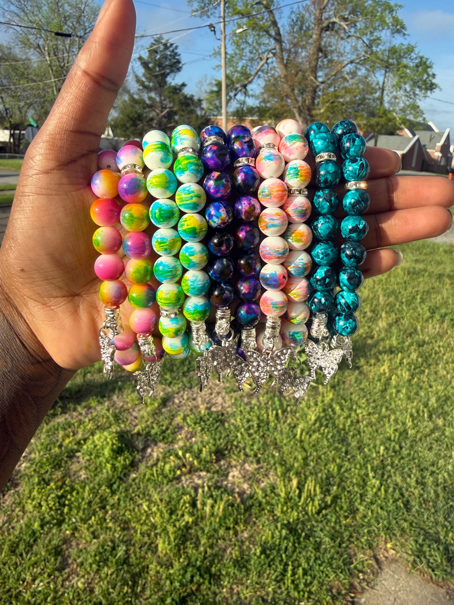 Hand holding a stack of colorful beaded bracelets with a blurred natural background