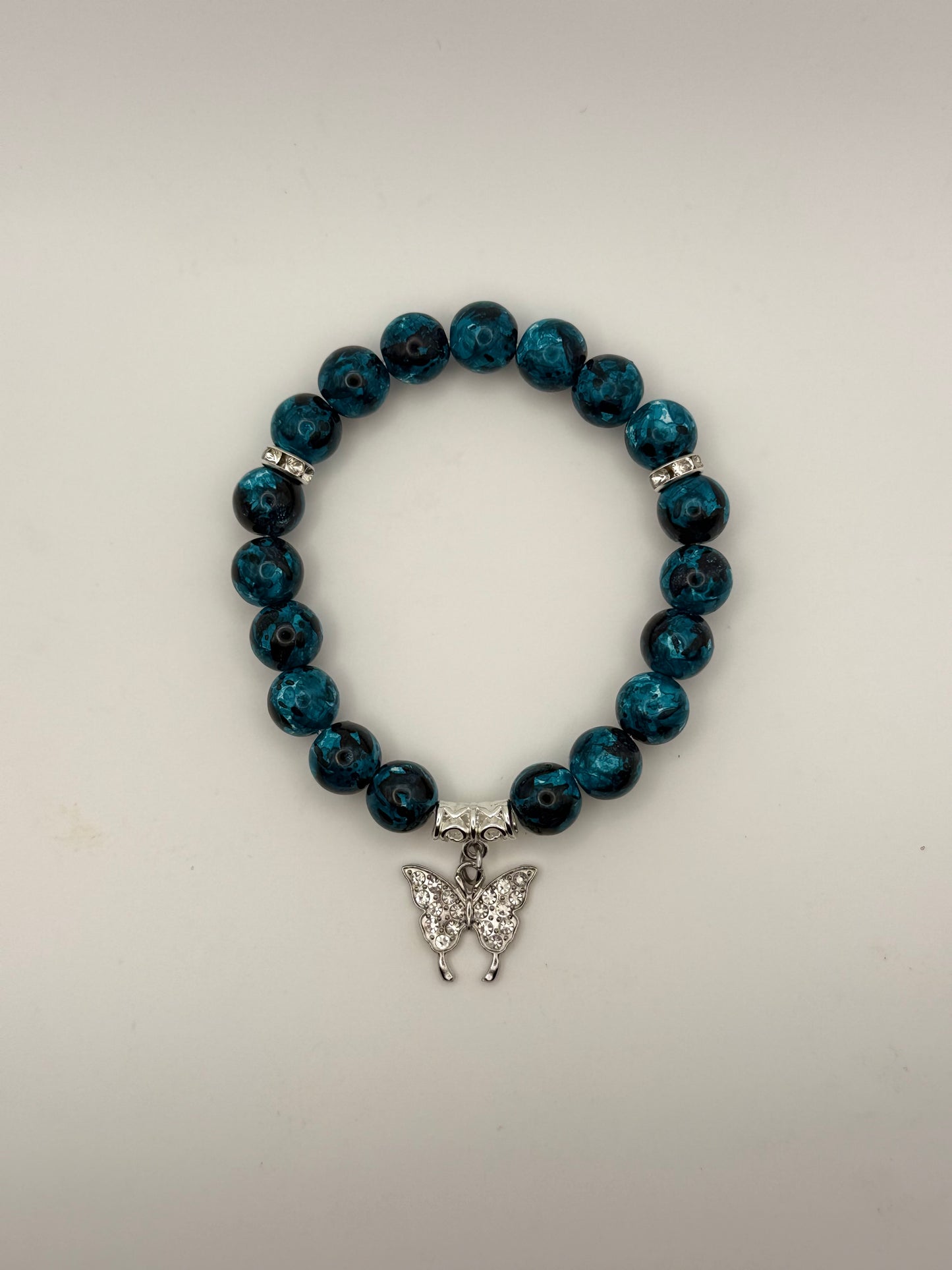 Blue beaded bracelet with a silver butterfly charm on a light gray background