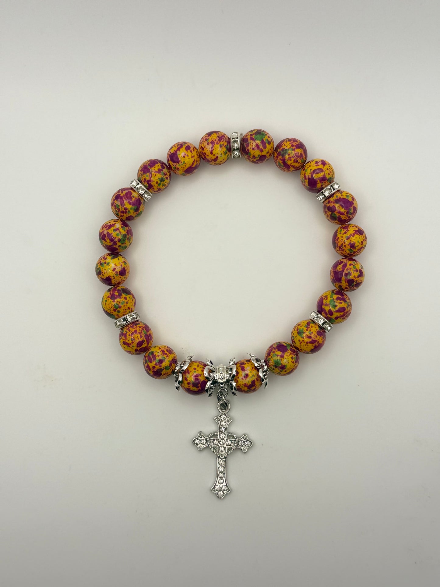 Bracelet with colorful beads and a silver cross charm on a light gray background